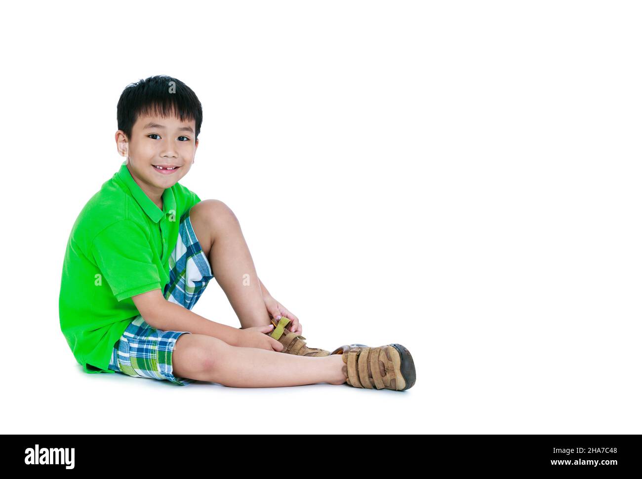 Corpo pieno di bambino asiatico carino sorridente e mettere scarpe in pelle su. Ragazzo felice seduto sul pavimento. Isolato su sfondo bianco e spazio libero per la copia. STU Foto Stock