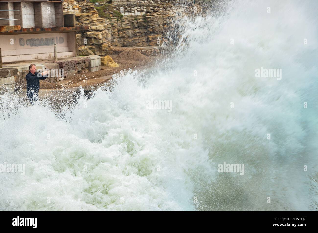 Uomo che fotografa mare tempestoso quasi inghiottito da onda gigante sul fronte mare di Scarborough Foto Stock