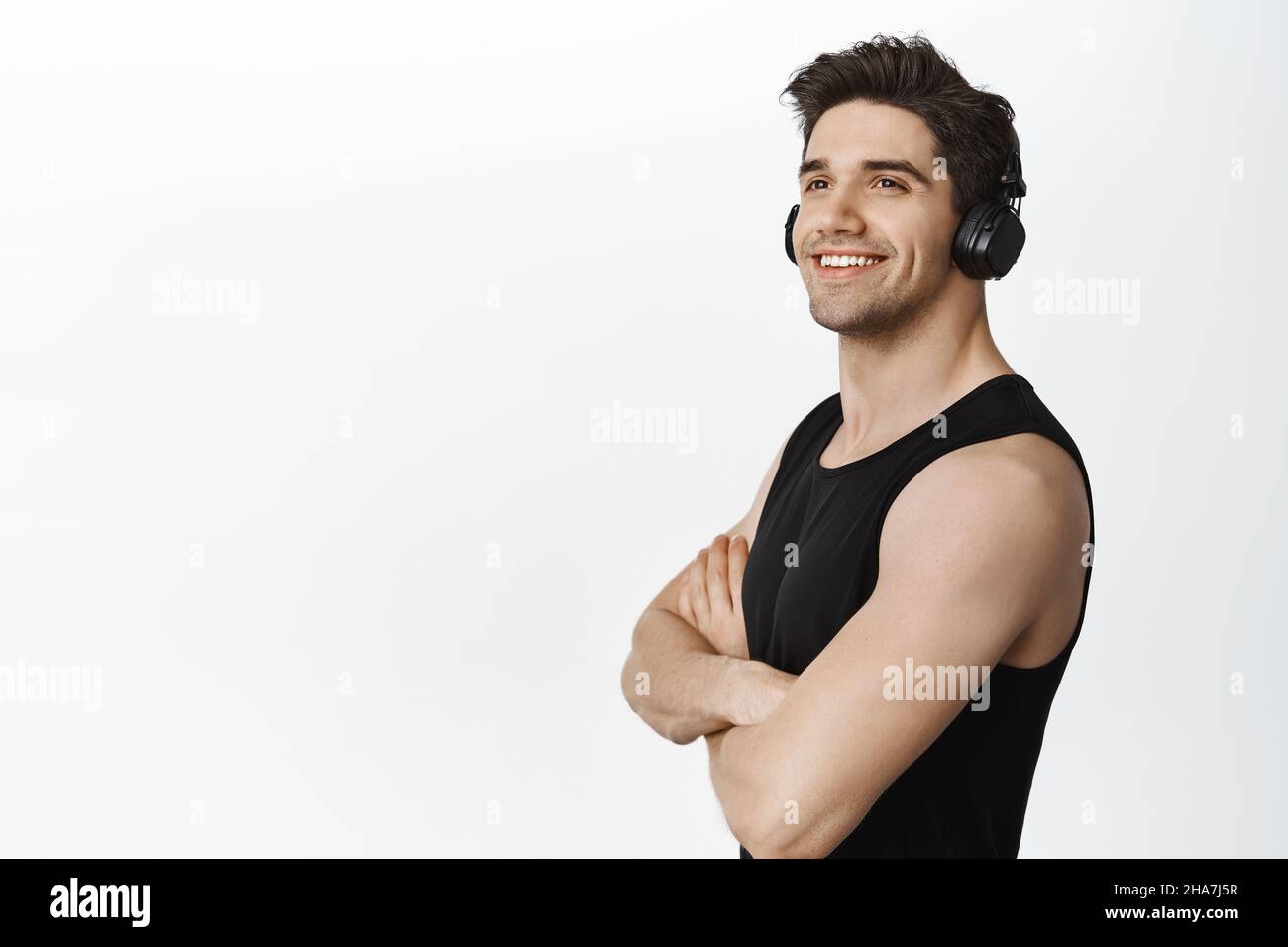 Istruttore di fitness forte e sicuro, uomo in palestra con cuffie, ascolto di musica e allenamento, in piedi su sfondo bianco con soddisfazione Foto Stock