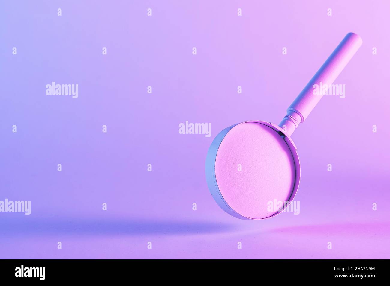 Spettacolare immagine a due tonalità di una lente di ingrandimento fluttuante su sfondo graduato rosa-blu con copyspace Foto Stock