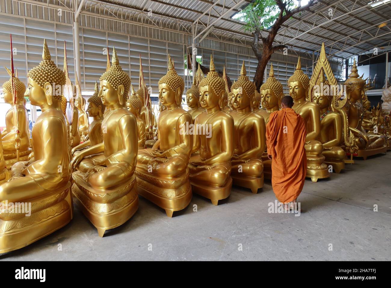 Sorridendo monaco buddista passa statue di Buddha in una fabbrica per l'acquisto di oggetti religiosi in Bambung Muang Road, Bangkok, Thailandia, Foto Stock