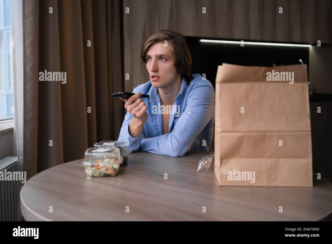 Giovane uomo con voce assistente ordinare cibo in cucina a casa, cibo da asporto pranzo sano, mangiare sano a casa in quarantena Foto Stock
