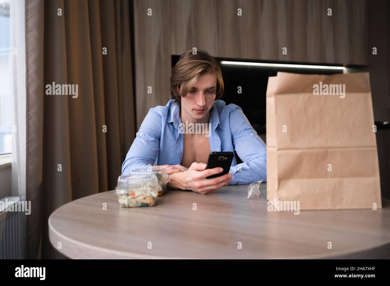 Ordinazione di cibo online, uomo con smartphone ordinazione di cibo da ristorante, pacchetto di cibo da asporto in cucina a casa, scatole da pranzo con verdure Foto Stock