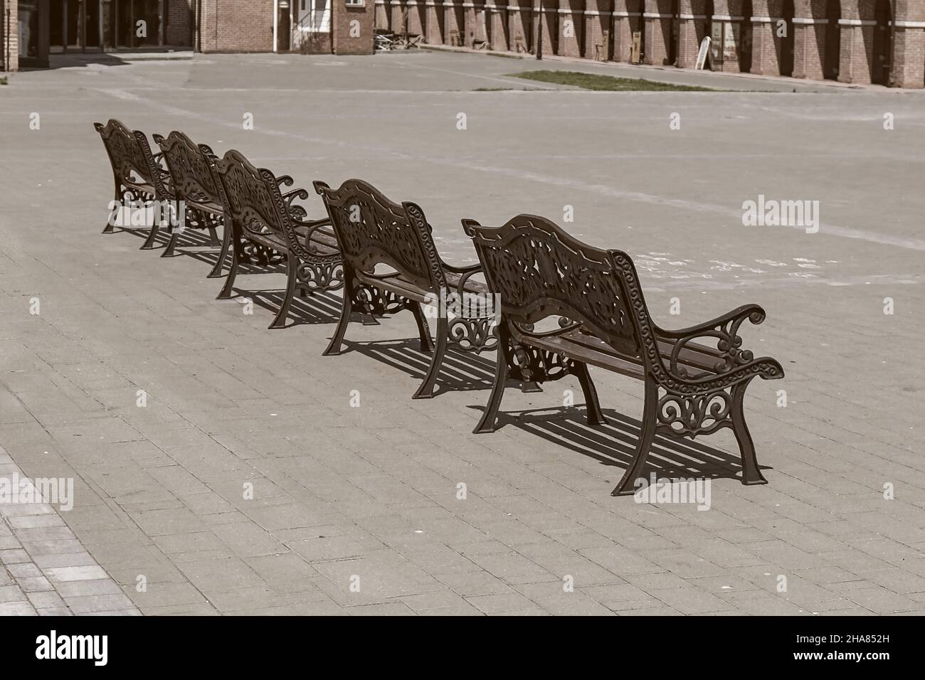 Fila di banchi in legno vintage vuoti con elementi ornati in ferro nero forgiato in tonalità seppia. Urban public vandal proof mobilio.Public area di riposo della città Foto Stock