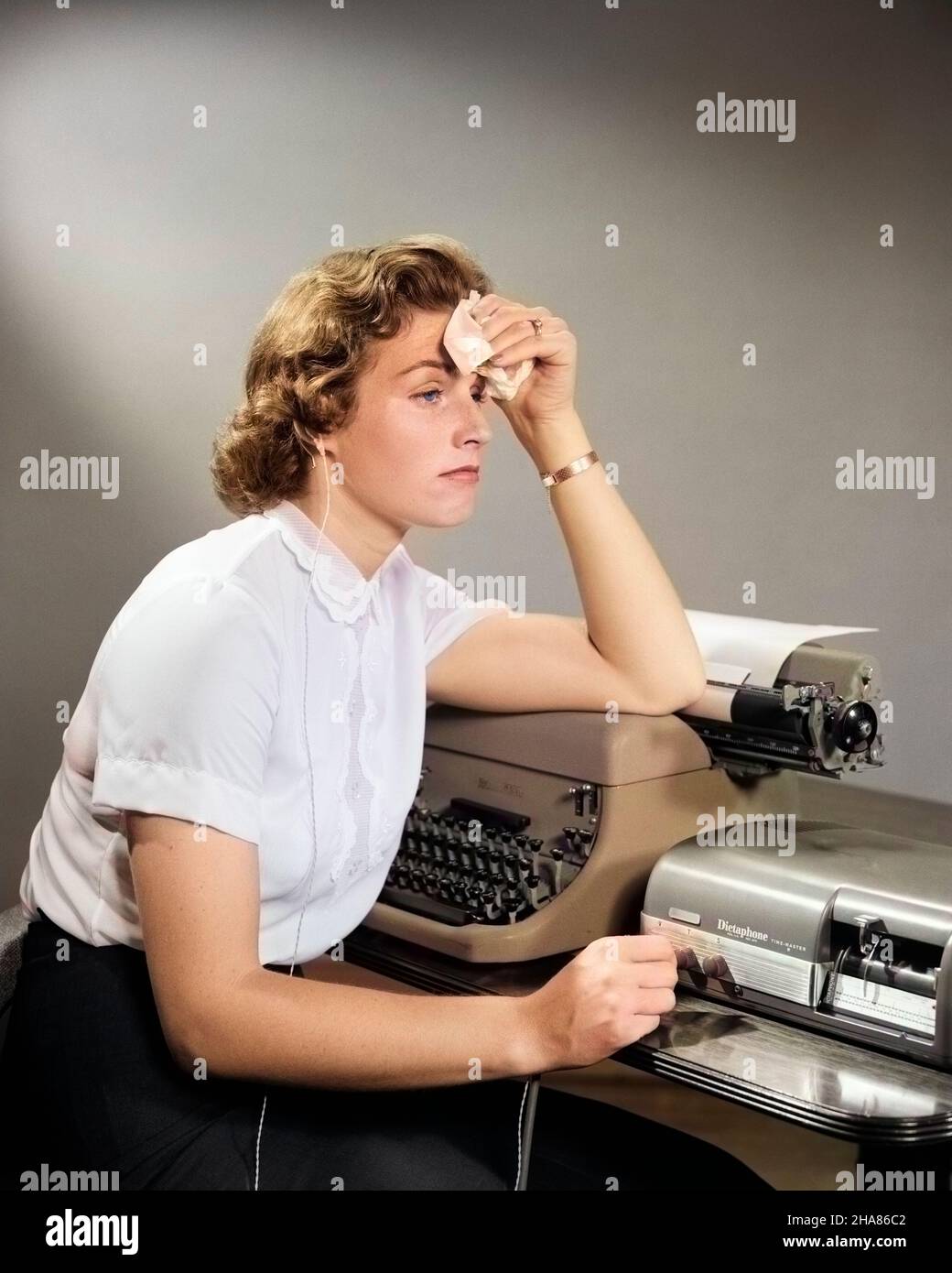 1950S SEGRETERIA DONNA IN DIFFICOLTÀ SEDUTA ALLA SCRIVANIA CON MACCHINA DA SCRIVERE E DETTATURA CHE TIENE IL FAZZOLETTO ALLA FRONTE - A2102C HAR001 HARS GROWNUP COPIA SPAZIO MEZZA LUNGHEZZA SIGNORE FISICA FITNESS PERSONE ADULTO-UP FRONTE CALDO MAL DI TESTA DISTURBATO PREOCCUPATO TRISTEZZA STROFINARE DICTAPHONE UFFICI WELLNESS PULIZIA OCCUPAZIONI DI UMORE MACCHINA DI UFFICIO SI PREOCCUPA PONDER MEDITARE GLUM NOIOSO SEGRETARI TESTA DOLORE DETTATURA METÀ-ADULTO DONNA MISERABILE SOPRA HA LAVORATO NOIA PREOCCUPANTE ETNIA CAUCASICA HAR001 VECCHIO STILE SURRISCALDATO Foto Stock