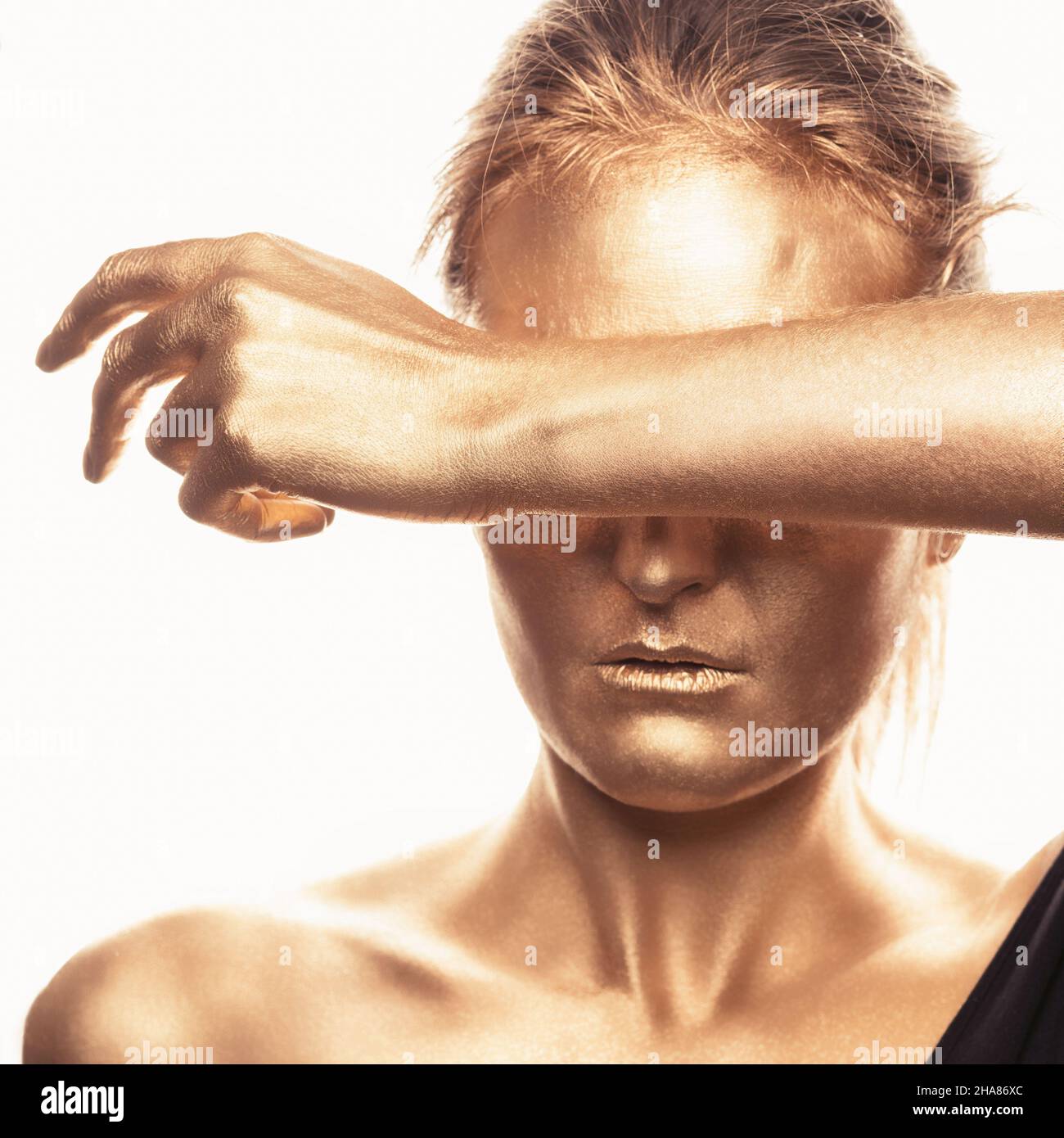 Bella donna dipinta d'oro, coprendo gli occhi con il braccio sollevato Foto Stock