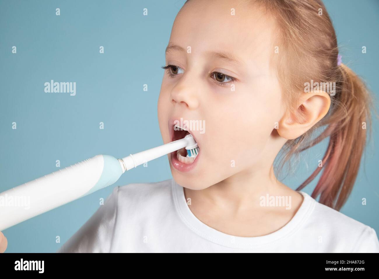 Adorabile bambino caucasico spazzolando denti in piedi su sfondo blu, concetto di igiene Foto Stock