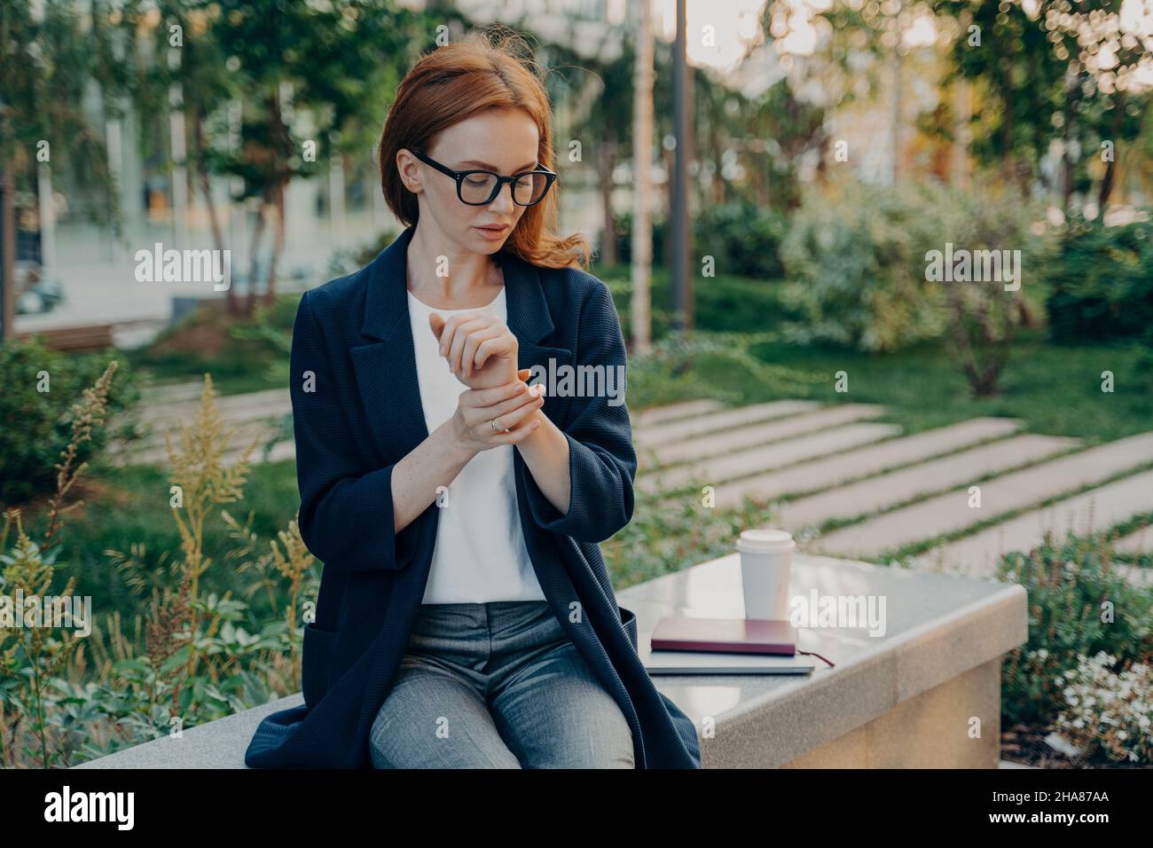 Giovane donna da lavoro rossa stanca che misura il polso sul polso, controlla la frequenza cardiaca, seduto nel parco Foto Stock