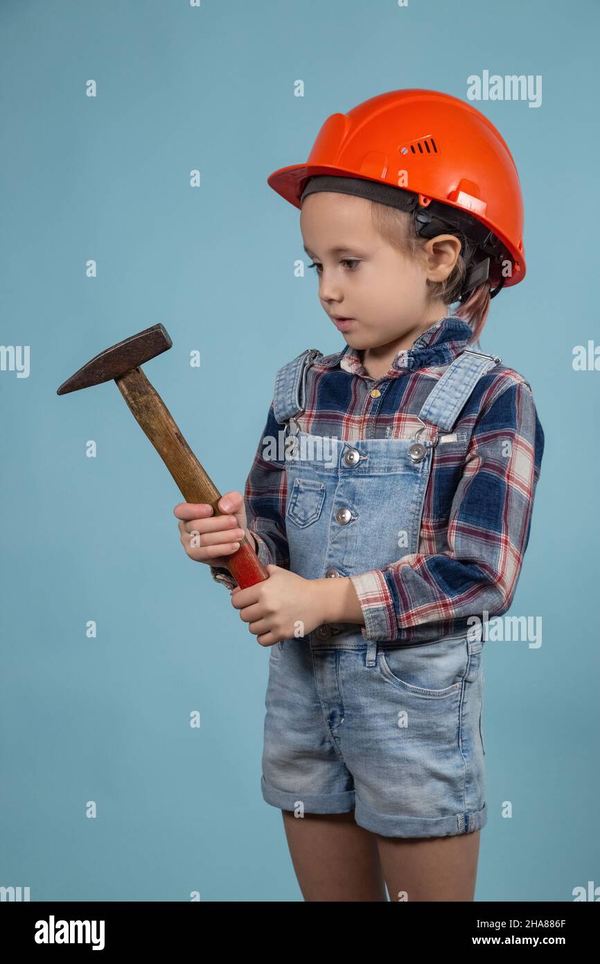 L'adorabile bambino caucasico indossa un casco di sicurezza arancione, tenendo il martello a mani. Concetto di costruzione di una casa per una famiglia felice Foto Stock