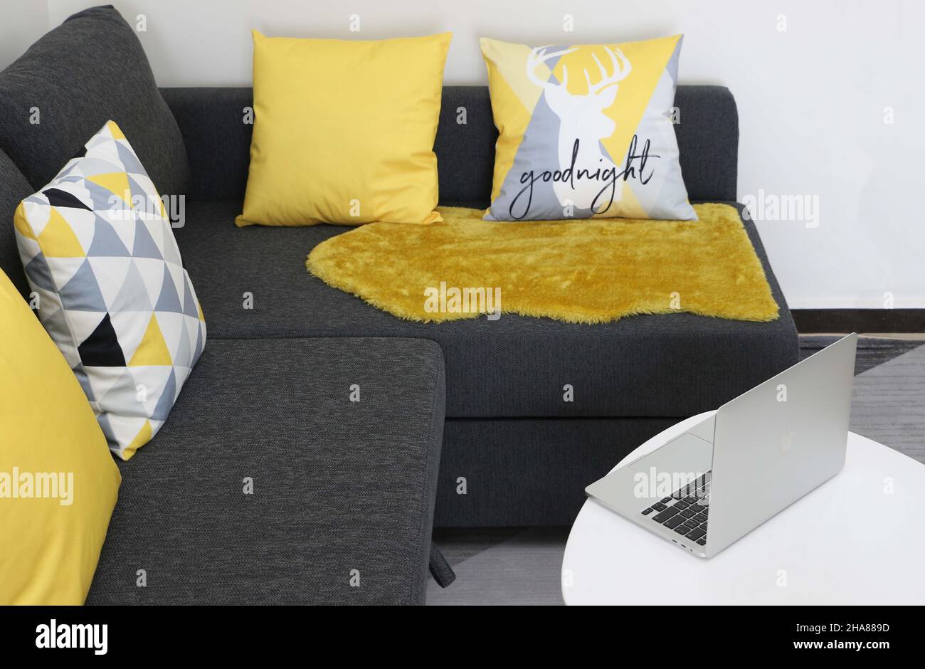 Caratteristiche del soggiorno di casa, MacBook Pro argento aperto sul tavolo da comodo divano grigio con cuscini gialli e a motivi geometrici Foto Stock