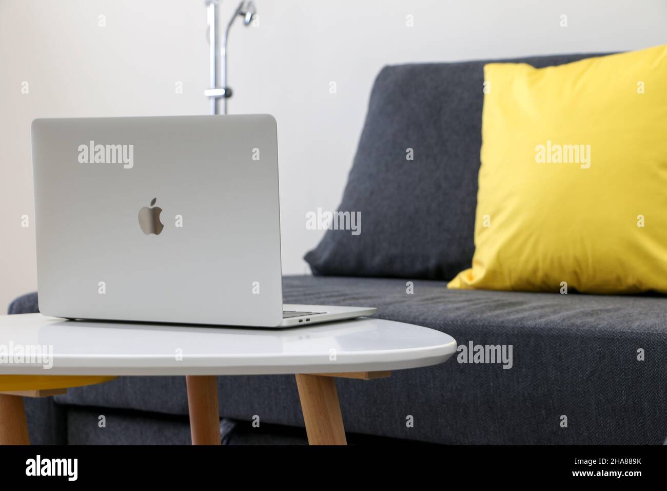 Lavora da casa pic, apri il laptop MacBook Pro su un tavolo bianco da un divano vuoto grigio con cuscino giallo Foto Stock