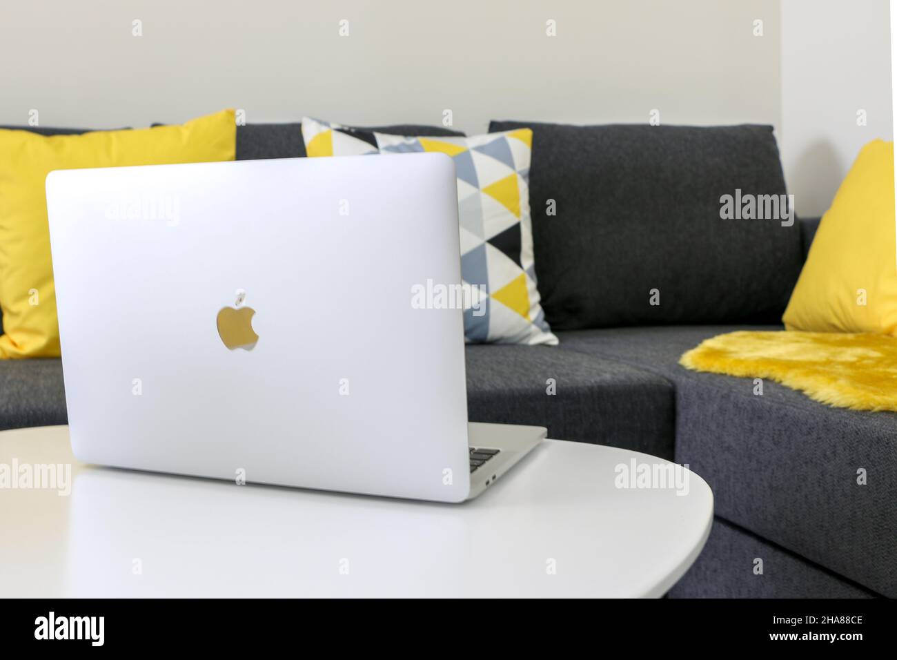 Apri il laptop MacBook Pro su un tavolo bianco di legno da un comodo divano grigio con cuscini Foto Stock