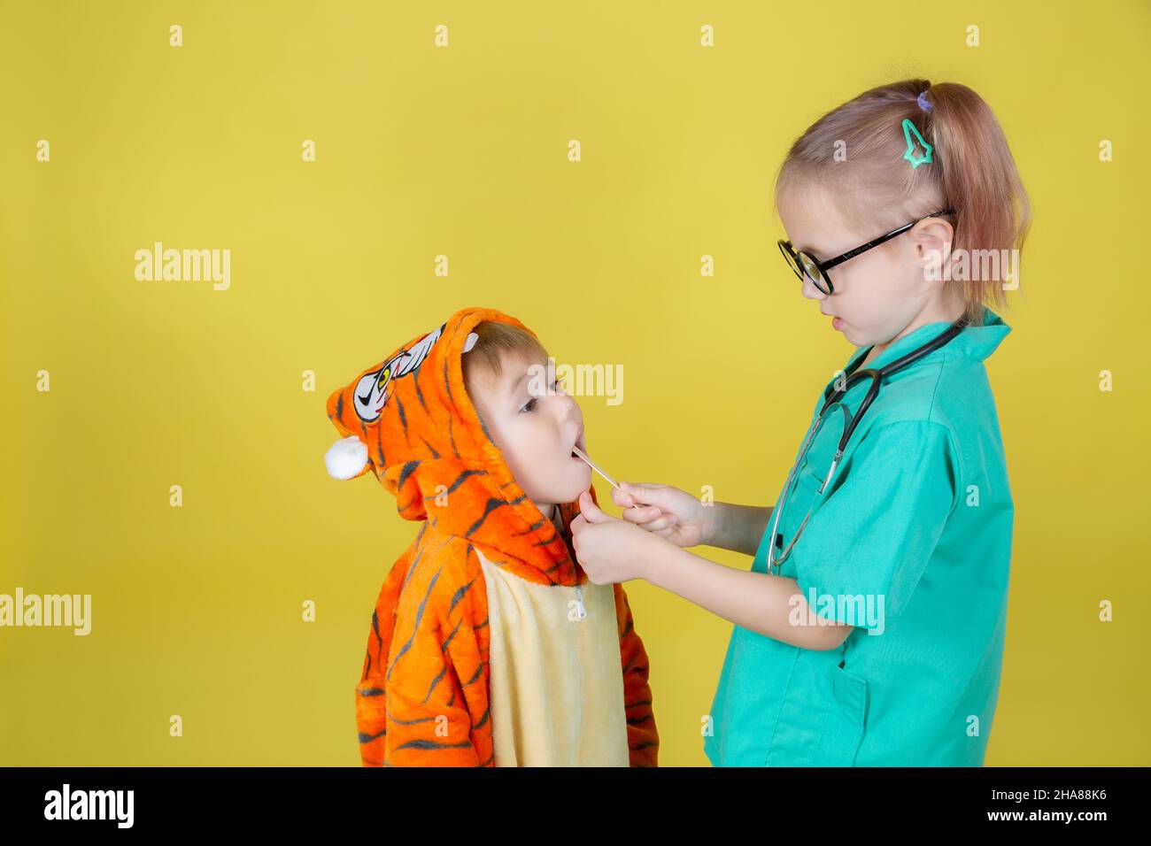 Piccolo caucasico bambini giocare medico, ragazzo in costume tigre mostra gola al pediatra su appuntamento medico Foto Stock
