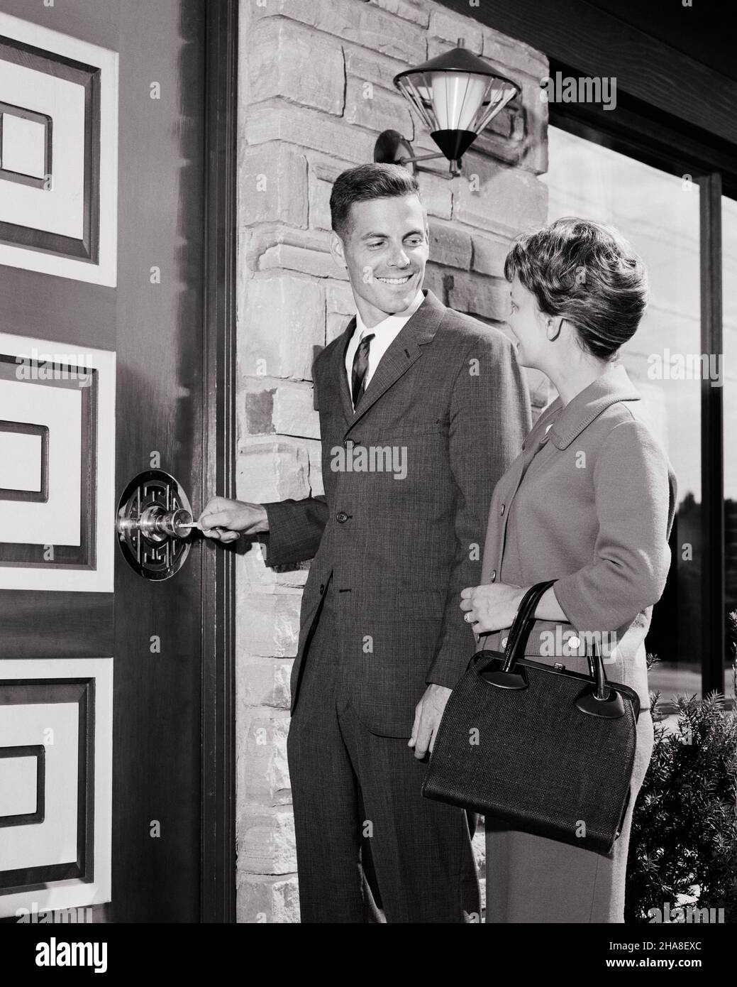 1960S GIOVANE COPPIA ALLA PORTA D'INGRESSO DEL NUOVO UOMO CASA MODERNA DI METÀ SECOLO SORRIDENDO A DONNA MENTRE SBLOCCANDO LA PORTA A. LORO NUOVA CASA - S14217 HAR001 HARS STILE BENVENUTO RIDERE LAVORO DI SQUADRA DESIGN FELICE GIOIA LIFESTYLE SODDISFAZIONE ARCHITETTURA FEMMINE CASE SPOSATE CONIUGE MARITI MODERNA HOME VITA COPIA SPAZIO AMICIZIA MEZZA LUNGHEZZA SIGNORE PERSONE RESIDENZIALI MASCHI EDIFICI FIDUCIA ESPRESSIONI B&W PARTNER OBIETTIVI SOGNI STRUTTURA FELICITÀ ALLEGRIA ECCITAZIONE ESTERNO BASSO ANGOLO ORGOGLIO CASE SORRISI GIOIOSO RESIDENCE PROPRIETARI DI CASA MID-ADULT UOMO MID-ADULT DONNA TOGETHERNESS SBLOCCO MOGLI Foto Stock