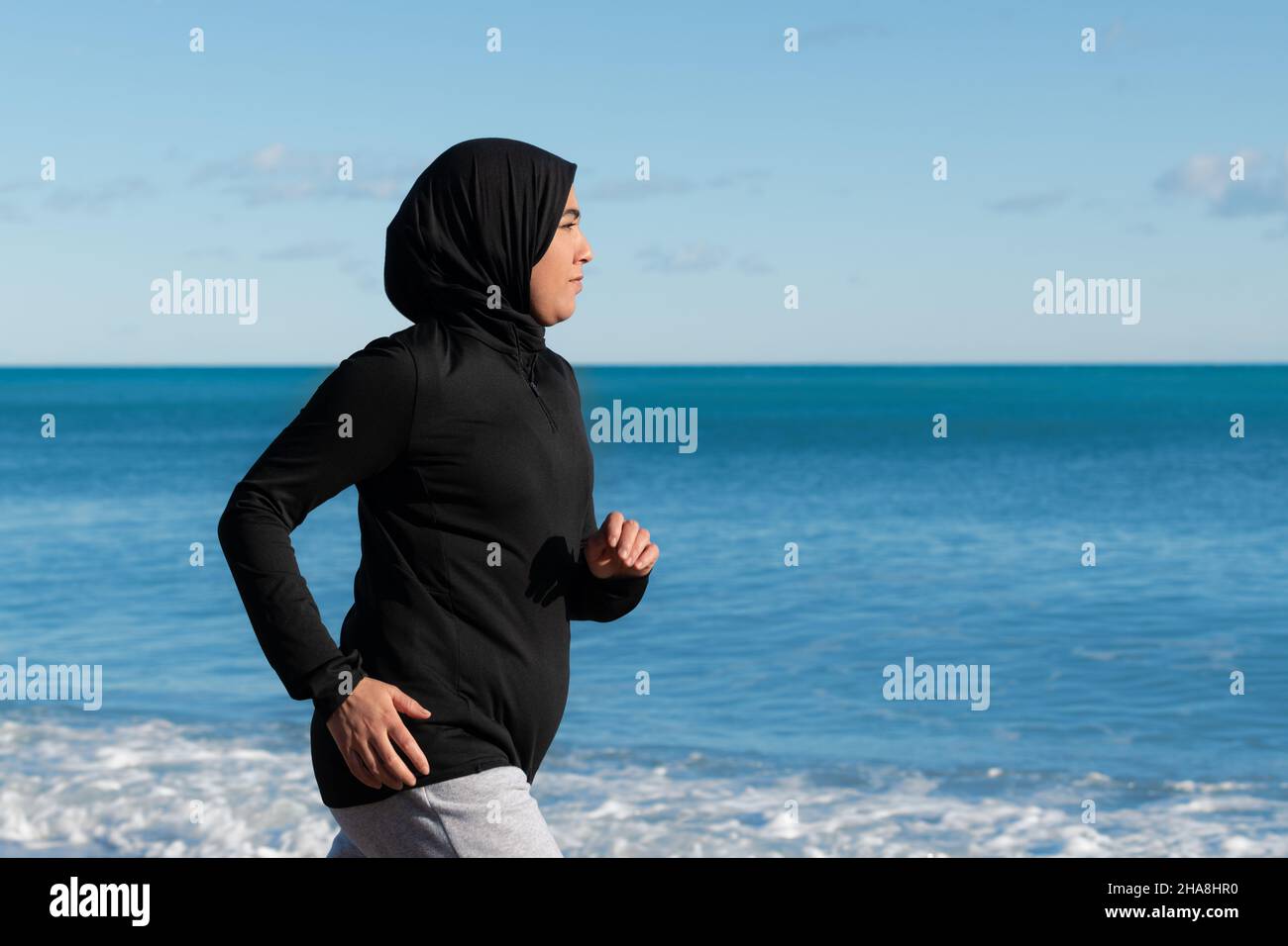 Donna araba che corre sulla spiaggia con il mare e l'orizzonte sullo sfondo Foto Stock