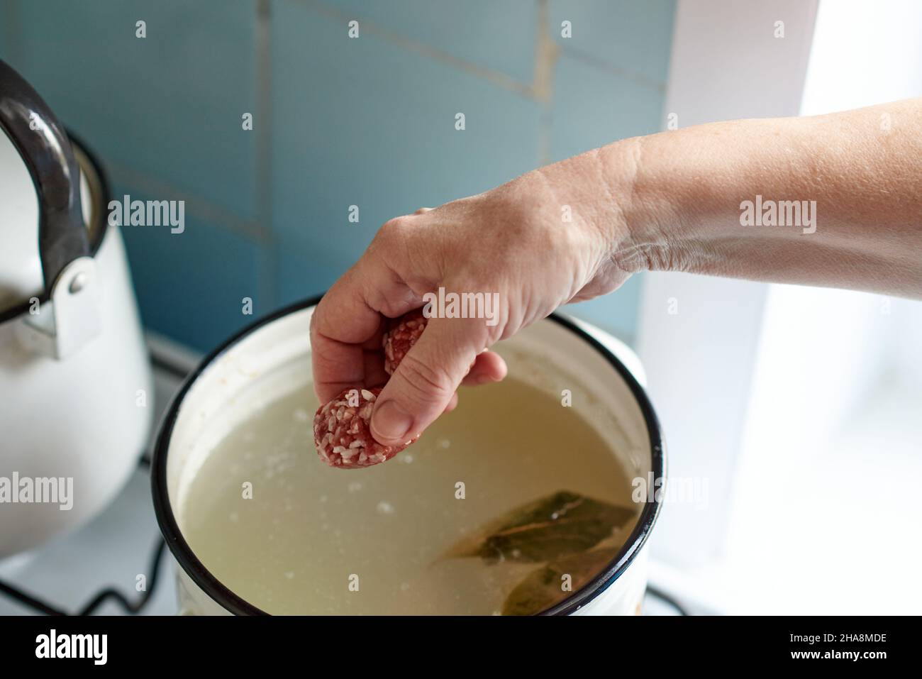 La mano di una donna lancia una palla a polpetta in una pentola di minestra bollente. Cucina casalinga sana. Foto Stock