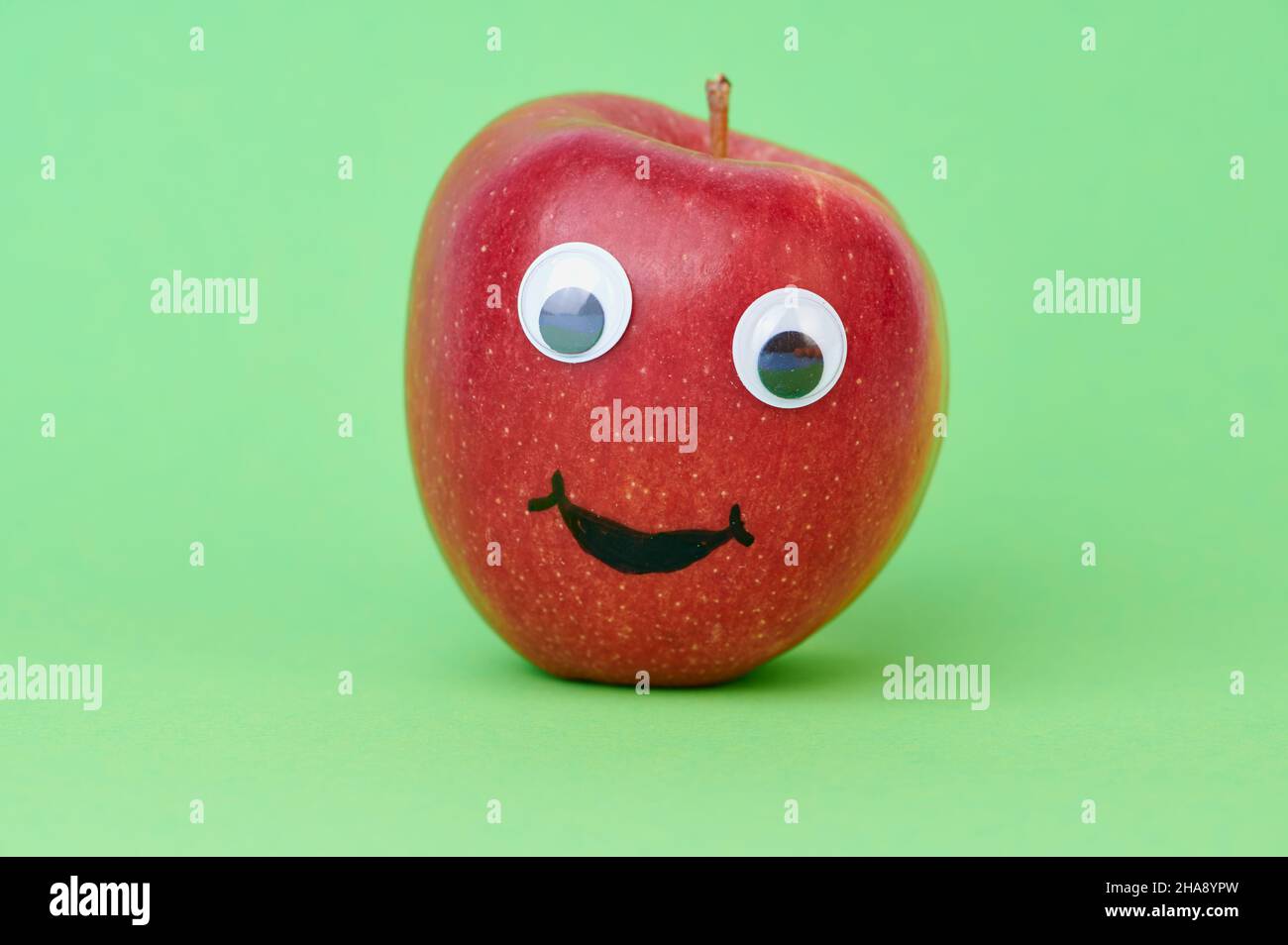 mela rossa con occhi ondeggianti su sfondo verde Foto Stock
