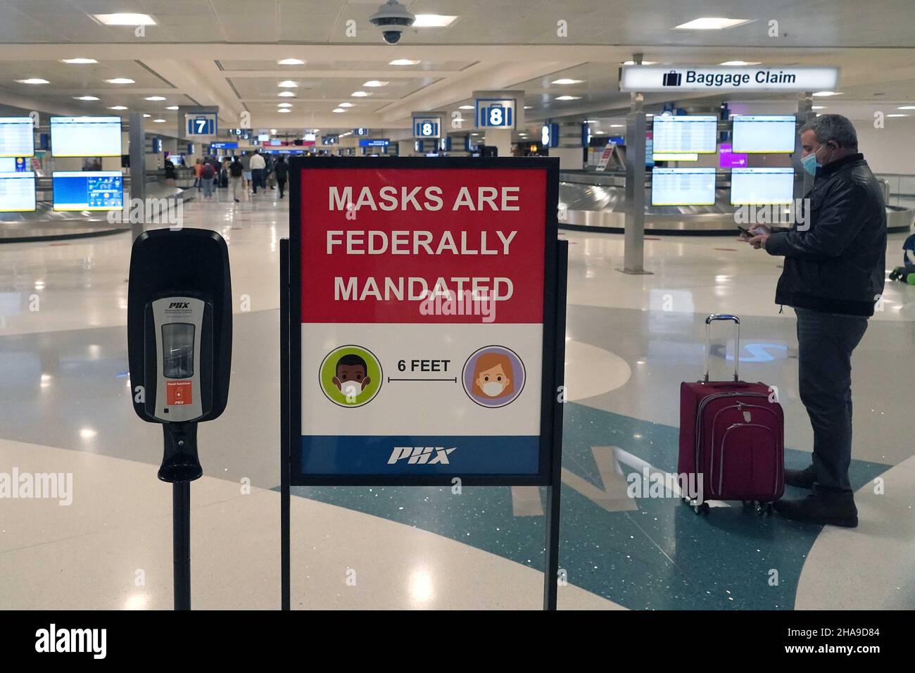 Un cartello con la maschera federale e un dispenser di disinfettante per le mani nell'area ritiro bagagli del terminal 4 dell'aeroporto internazionale Sky Harbor di Tuesda Foto Stock