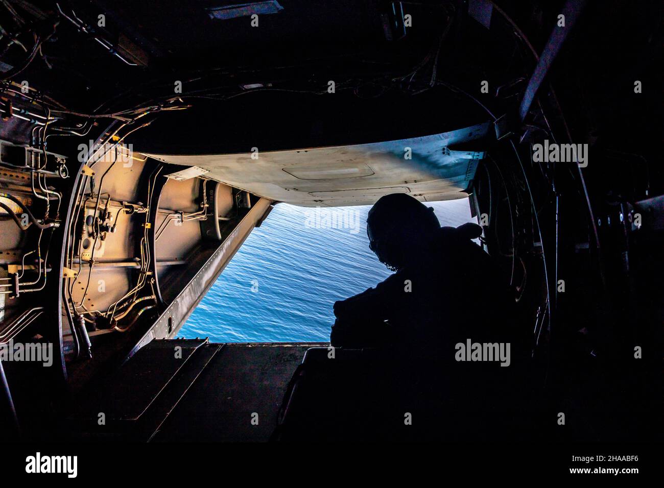 Una Marina degli Stati Uniti con Marine Medium Tiltrotor Squadron 364 (VMM-364), guarda verso l'esterno il retro di un MV-22B Osprey durante l'esercitazione Steel Knight 22 (SK-22), come vola sopra l'Oceano Pacifico, 5 dicembre 2021. SK-22 è un esercizio di addestramento annuale condotto dalla Marine Division del 1st che consente al team Navy-Marine Corps di operare in un ambiente realistico e a armi combinate per migliorare tattiche, tecniche e procedure di combattimento navale. (STATI UNITI Foto del corpo marino di CPL. Jacob Yost) Foto Stock