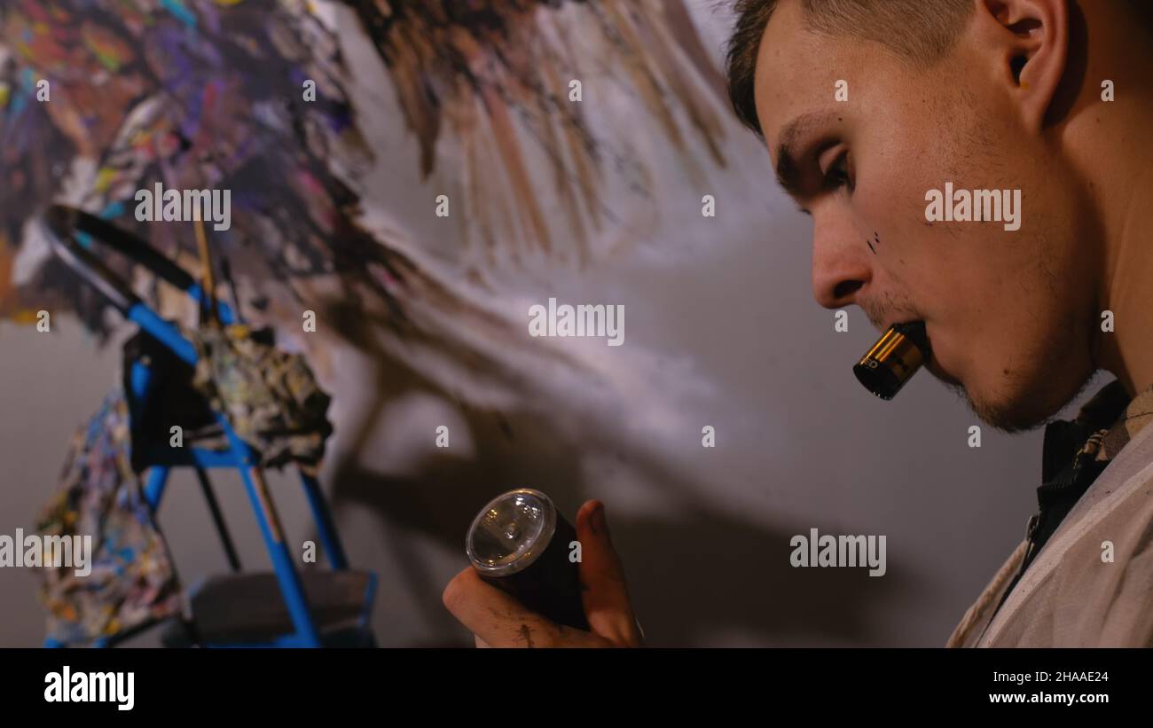 Artista designer disegna un aquila sulla parete. Artigiano arredatore dipinge un quadro con olio acrilico colore. Fumi Vaper vape. Pittore pittore vestito in Foto Stock
