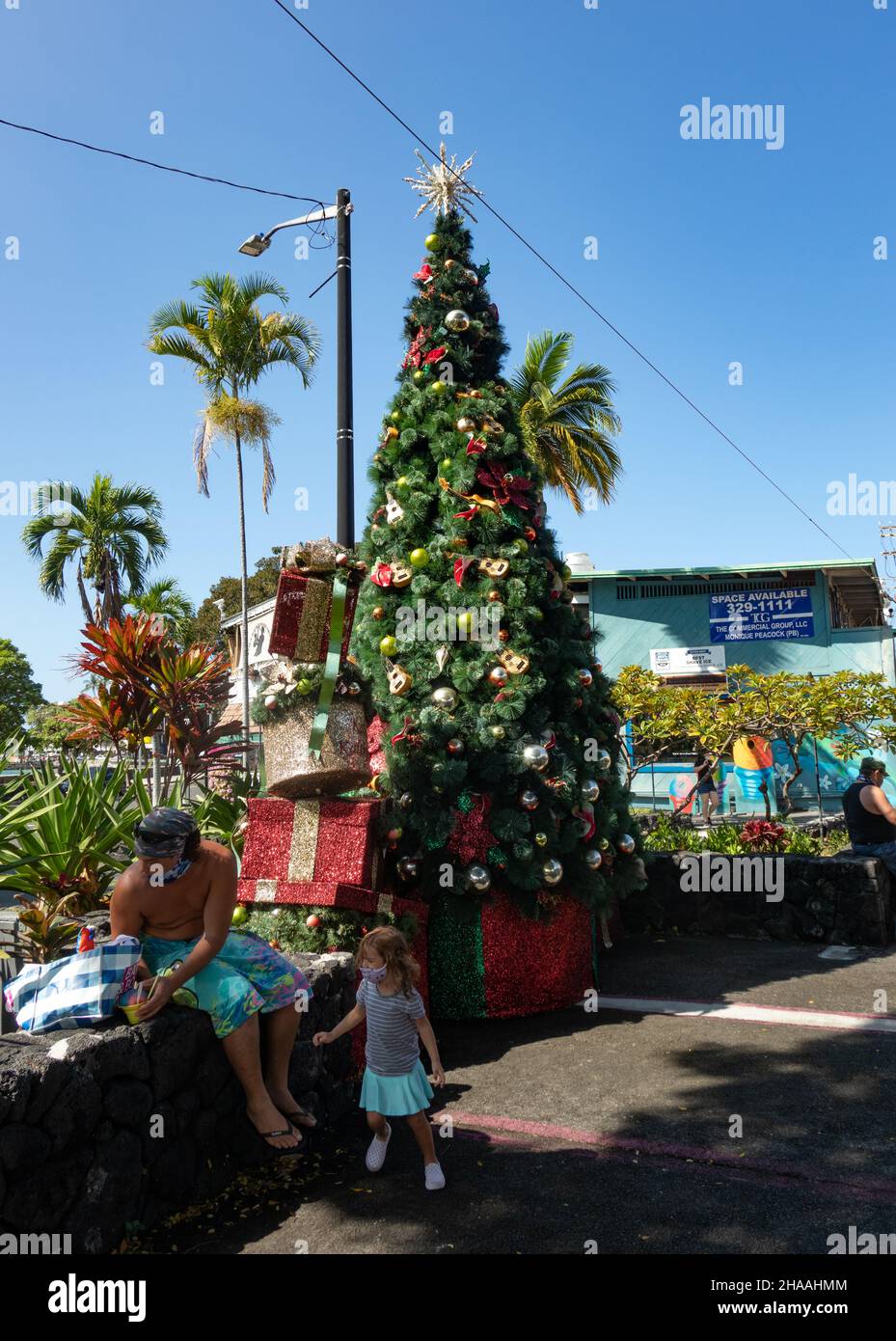 Un uomo e sua figlia si fermano per radere il ghiaccio vicino a un albero decorativo di Natale nel centro di Big Island. Foto Stock