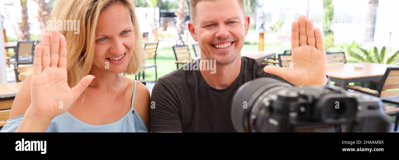 L'uomo e la donna sono seduti al tavolo nel bar e ondeggiano alla macchina fotografica Foto Stock