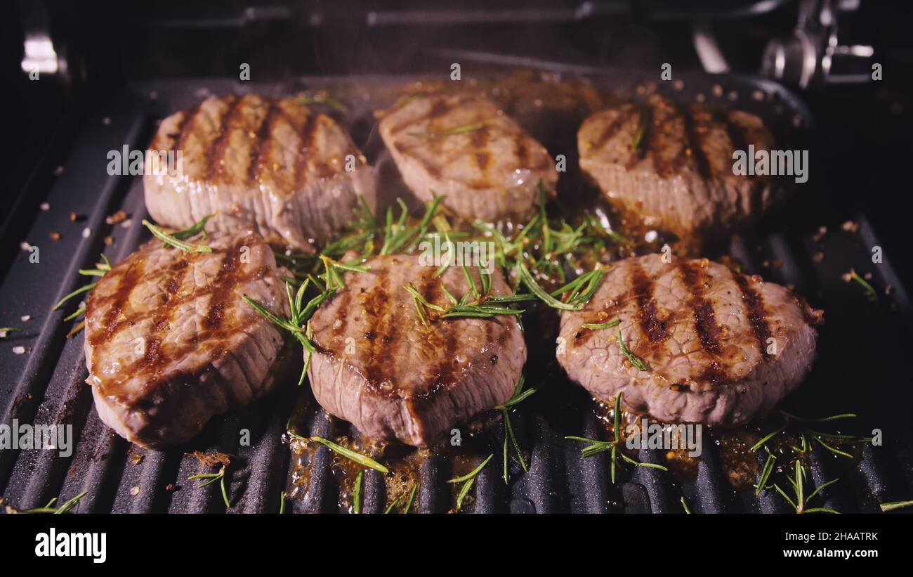 Deliziosa bistecca di carne succulenta cucinata alla griglia. Primi frittura di manzo su tostiera elettrica, rosmarino, pepe nero, sale. Movimento lento. Foto Stock