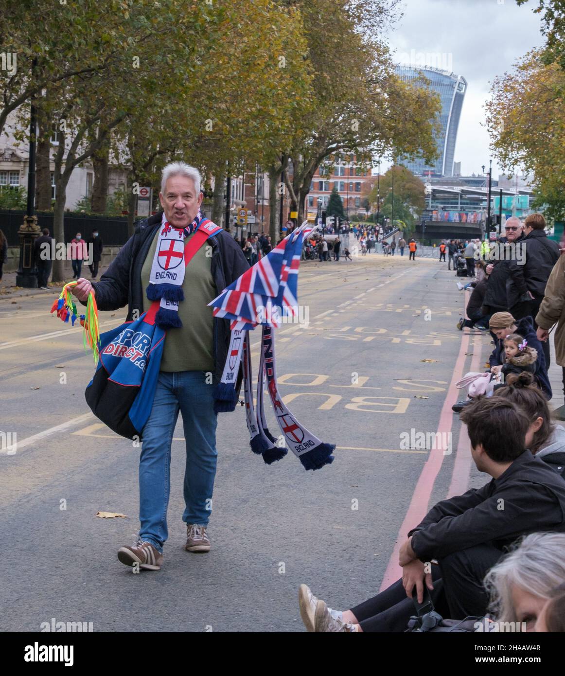Un uomo cammina lungo Victoria Embankment vendendo striscioni inglesi e bandiere britanniche prima del Lord Mayor’s Show, 2021. Walkie Talkie in background. Foto Stock