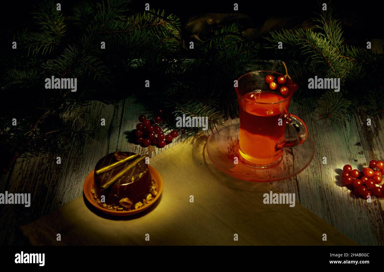 Composizione di pittura luce di Natale. Una tazza di tè di viburnum, cosparso, bacche di viburnum su un tavolo di legno con rami di albero di Natale nel backgro Foto Stock