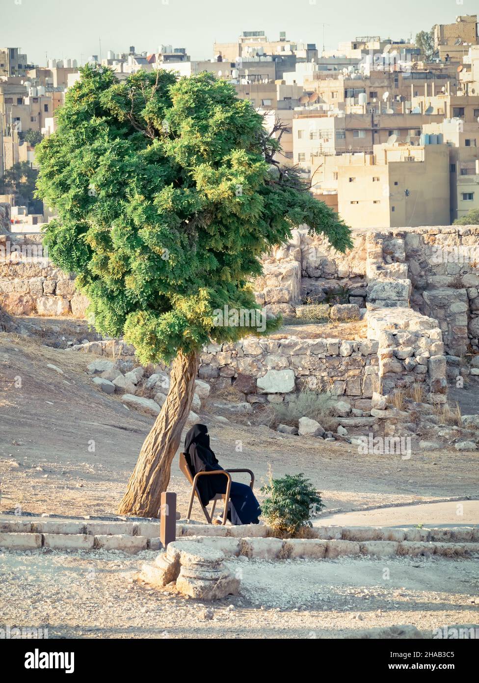 Donna araba su una panca nella Cittadella di Amman che indossa un abito nero tradizionale abaya Foto Stock