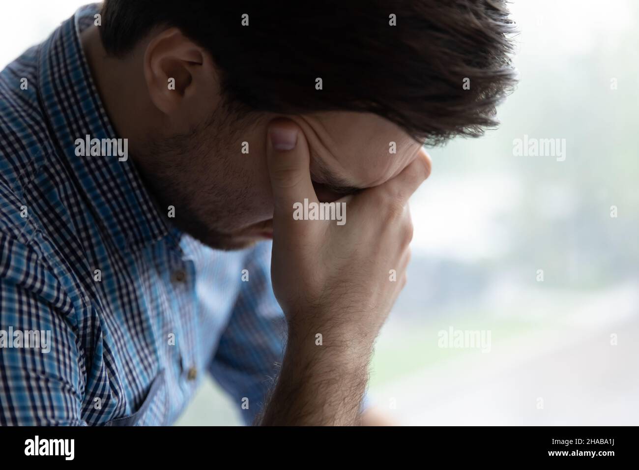 Triste uomo giovane senza speranza seduto da solo al coperto sembra disperato Foto Stock