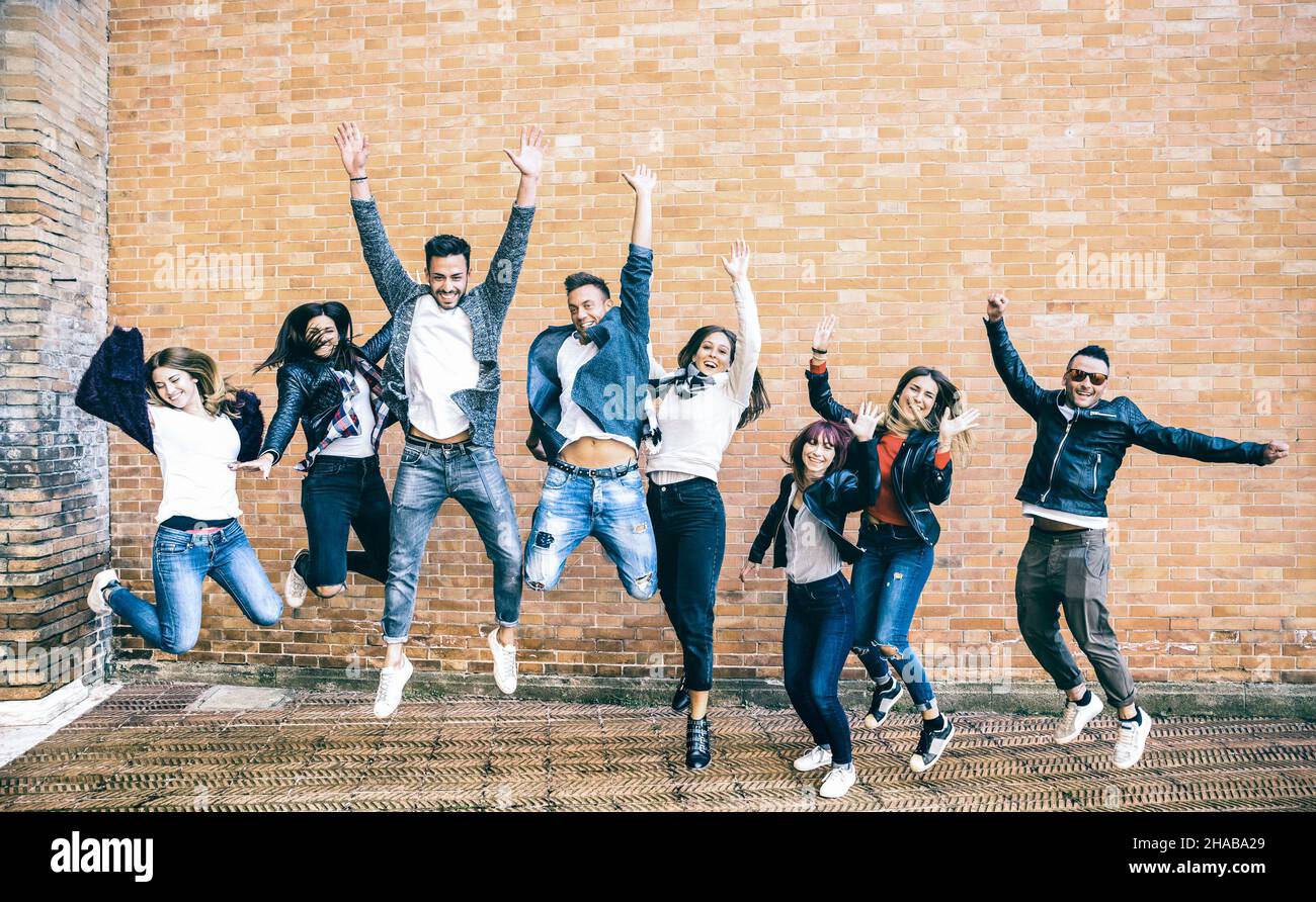 Amici felici i millennials saltano e si acclamano contro il muro di mattoni in città - stile di vita di amicizia e concetto di squadra con i millenni dei giovani Foto Stock