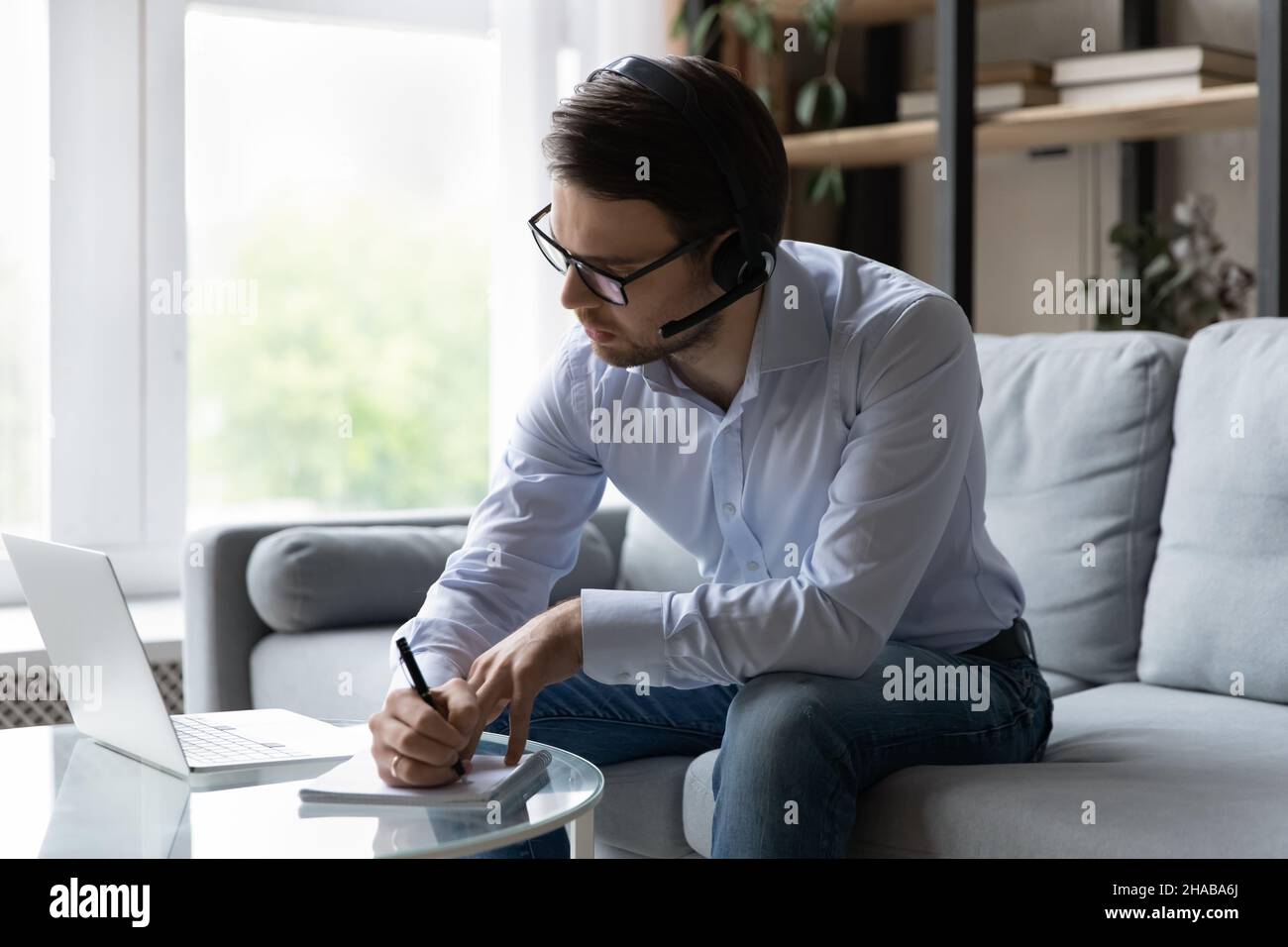 Giovane uomo d'affari indossare cuffie ascoltare audio corso scrive in copybook Foto Stock