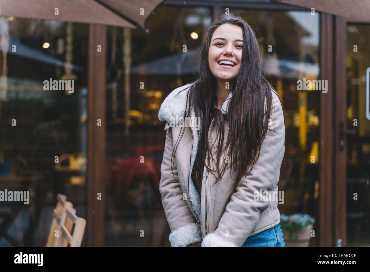 Bella donna sorridente con lunghi capelli indossando una giacca calda passeggiata lungo strada caldo inverno europeo. Protezione dei capelli dal freddo, trattamenti dei capelli. Foto Stock