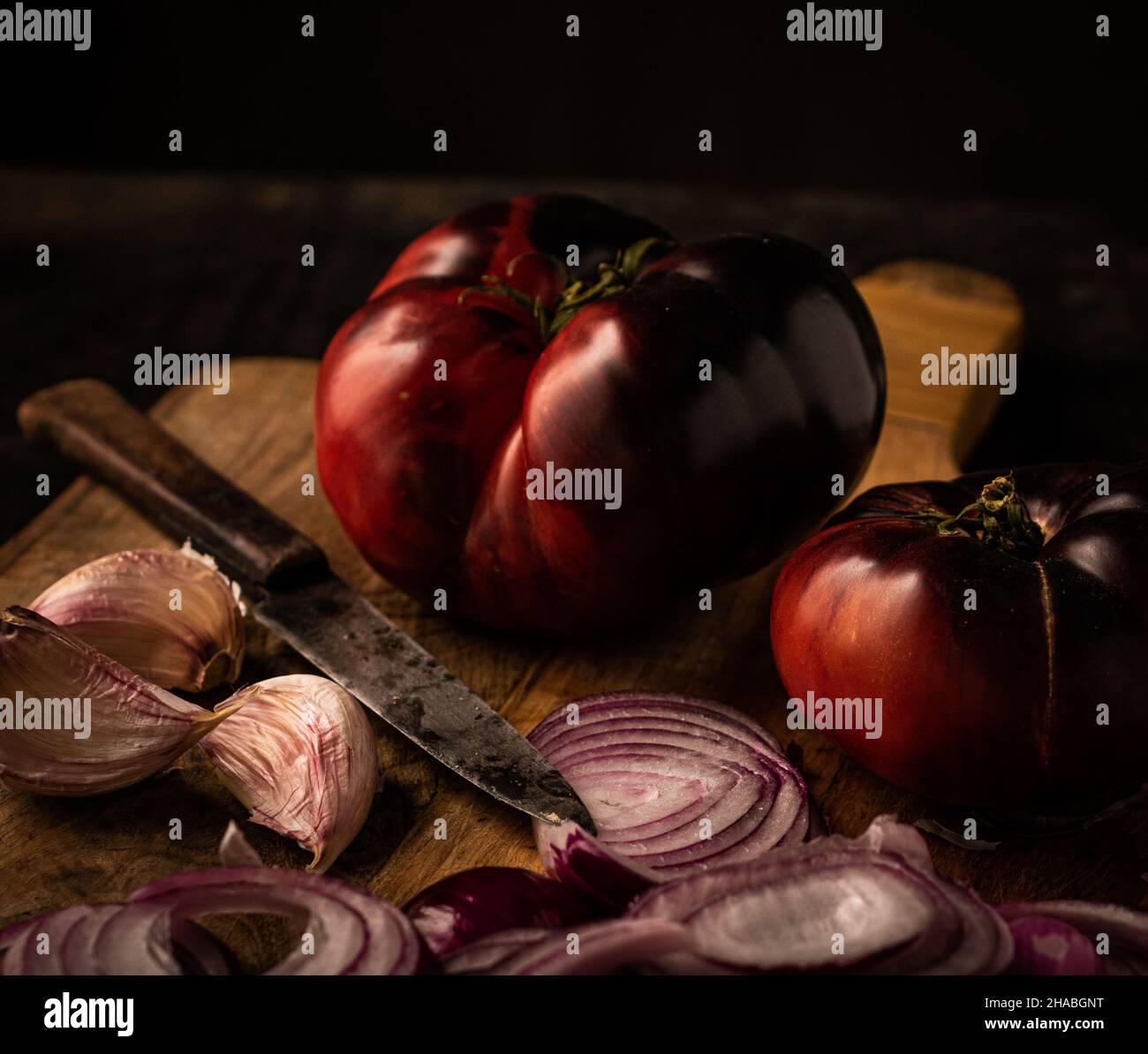 ancora vita di pomodoro blu di manzo, su un tagliere di legno e un po 'di aglio viola, cipolla rossa e un coltello Foto Stock