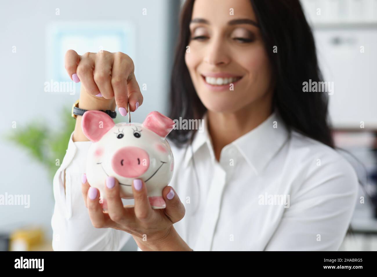 Donna felice che mette le monete in contenitore di piggybank e sorridente Foto Stock