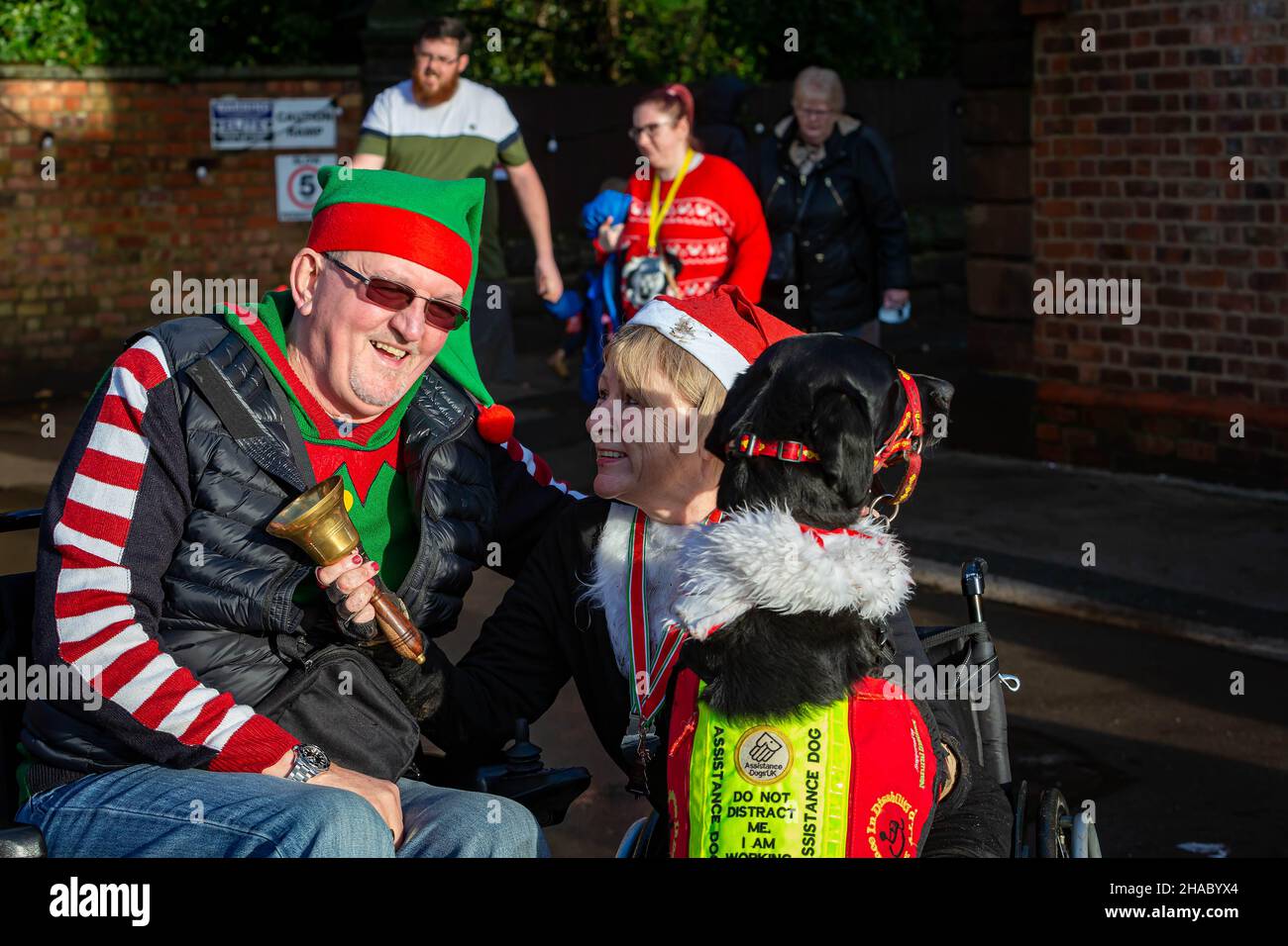 Warrington, Regno Unito. Domenica 12 Dicembre 2021 - Walton Hall and Gardens. Dopo una pausa di un anno, l'annuale Santa Dash/Santa Walk 3K organizzato dalla Warrington Disability Partnership anche se il tempo pioveva all'inizio. Dave Thompson MBE DL MBA si congratula con la signora, Jill Keast Doran, che ha completato 0,75K senza gambe come il suo cane di assistenza si unisce alle celebrazioni Credit: John Hopkins/Alamy Live News Foto Stock