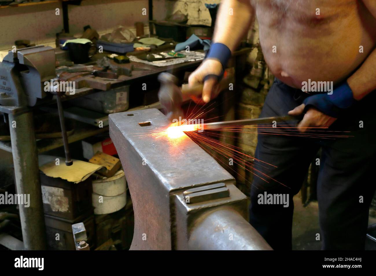 Un fabbro che lavora un pezzo di metallo redhot su un incudine nel processo di fabbricazione di un chiodo vecchio stile al Bradford Industrial Museum, West Yorkshire Foto Stock