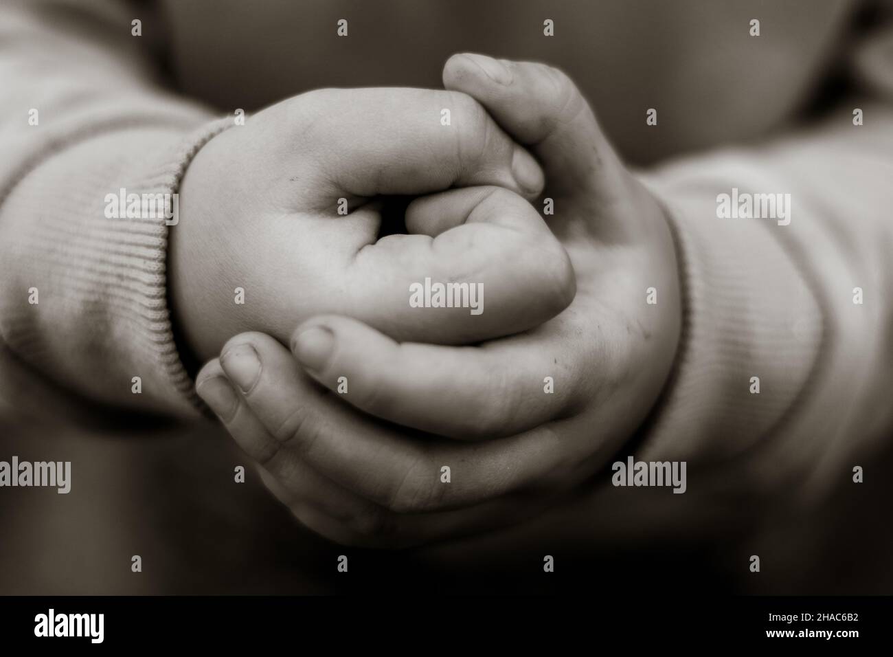 Il genitore tiene la mano di un bambino piccolo su sfondo sfocato astratto, fuoco morbido, tono bianco e nero Foto Stock