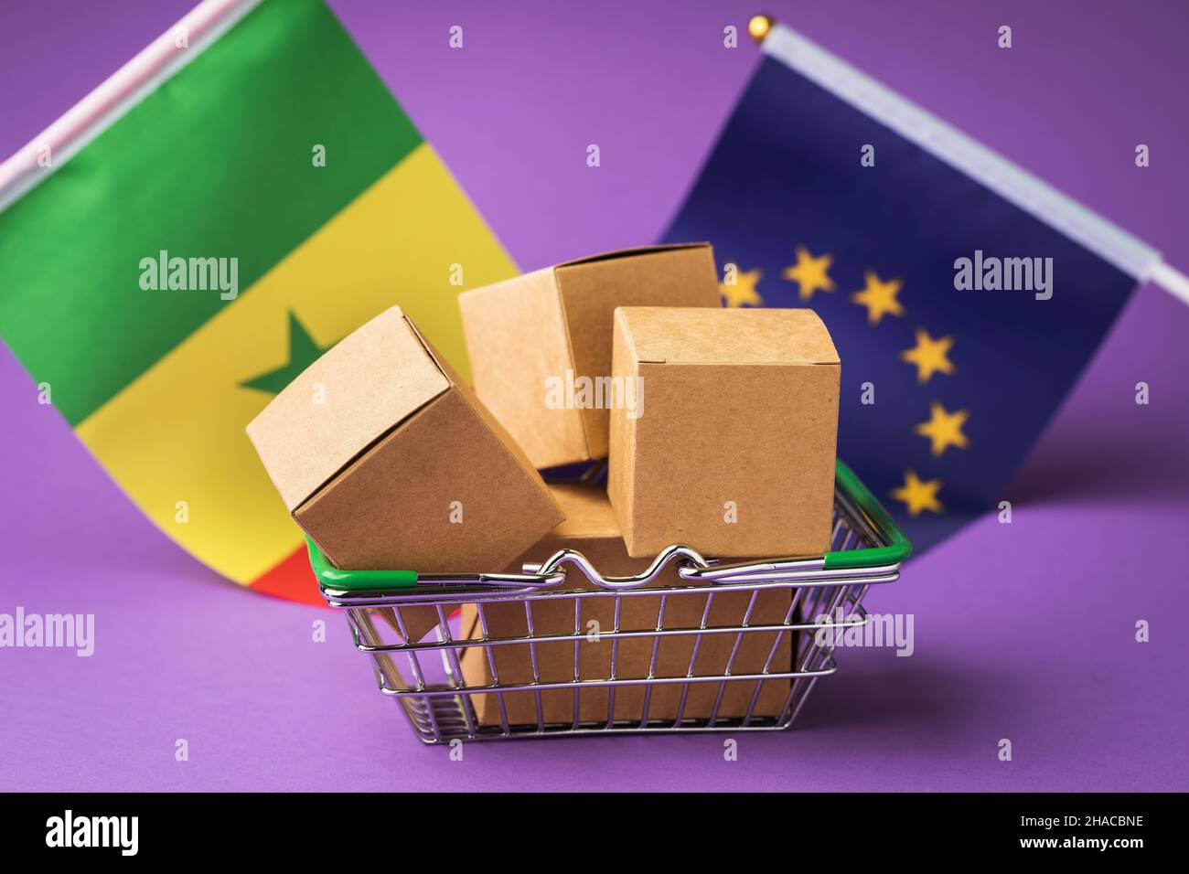 Scatole di cartone in un cestino alimentare e bandiere su sfondo colorato, il concetto di commercio tra l'UE e il Senegal Foto Stock