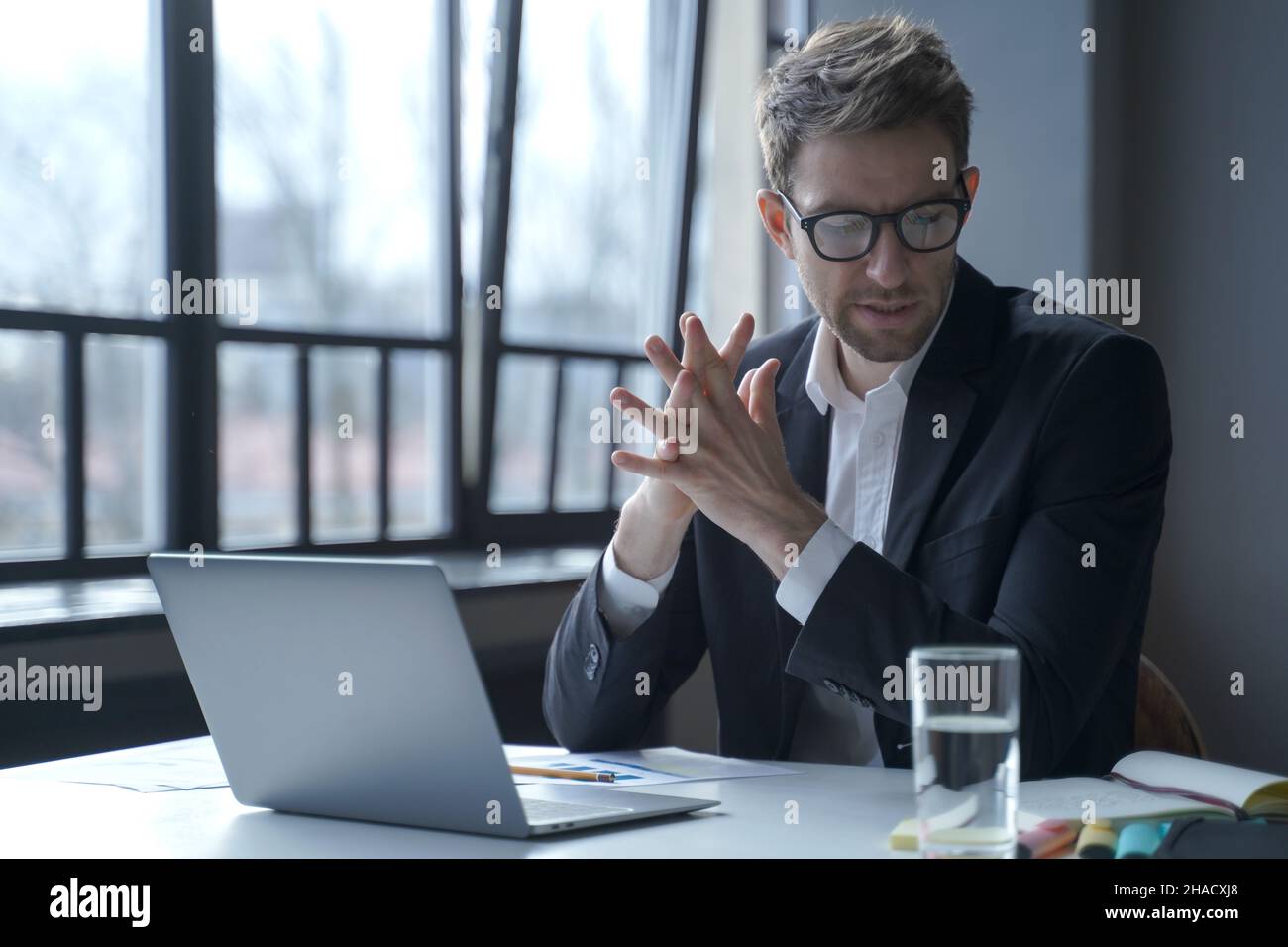 Brooding concentrato uomo d'affari tedesco in tuta formale e bicchieri seduti in ufficio Foto Stock