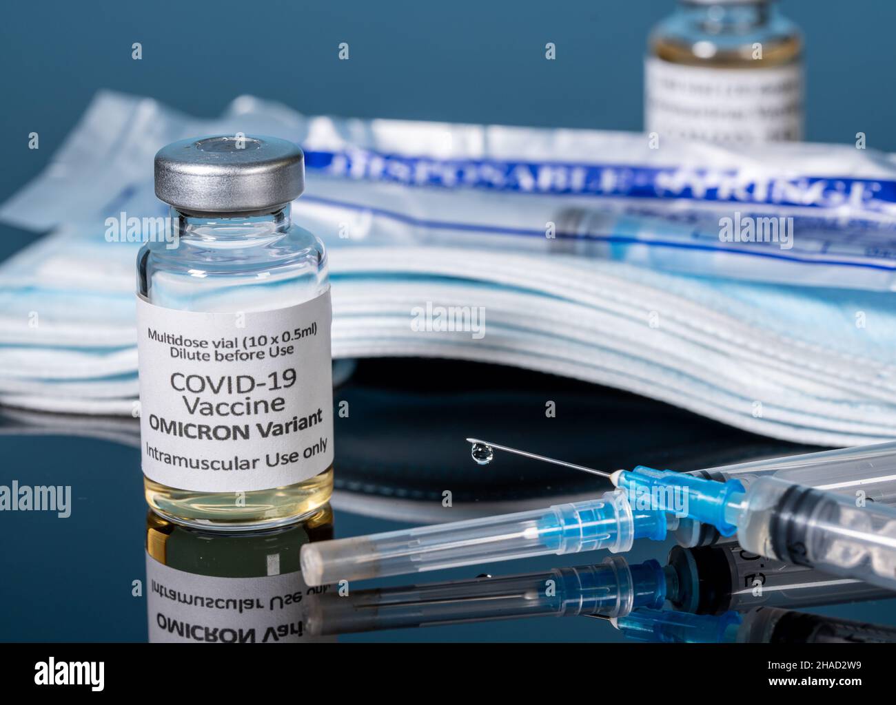 Vaccino per coronavirus Covid-19 sviluppato per la variante Omicron con ago per siringa ipodermica con maschere e nuove siringhe sullo sfondo Foto Stock