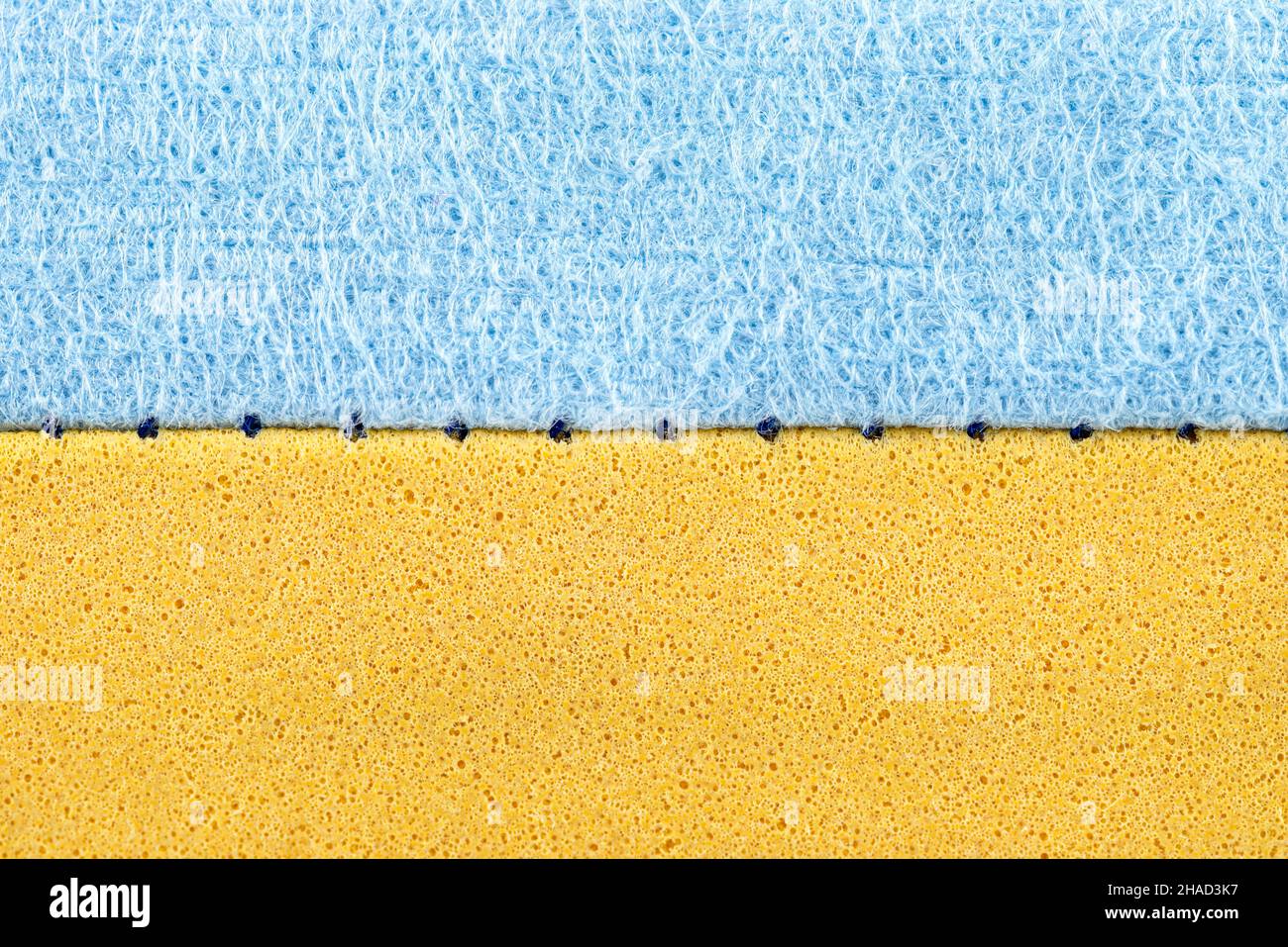 Sfondo realizzato da una macro foto di una spugna blu e gialla per il lavaggio di vetro e piatti, la cucitura è visibile. Foto Stock