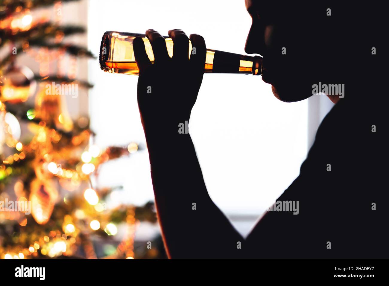 Problema di Natale e alcol. L'uomo solitario beve birra. Albero di Natale. Alcolismo da solo durante le vacanze. Sorseggia da una bottiglia di lager. Ragazzo triste con depressione. Foto Stock