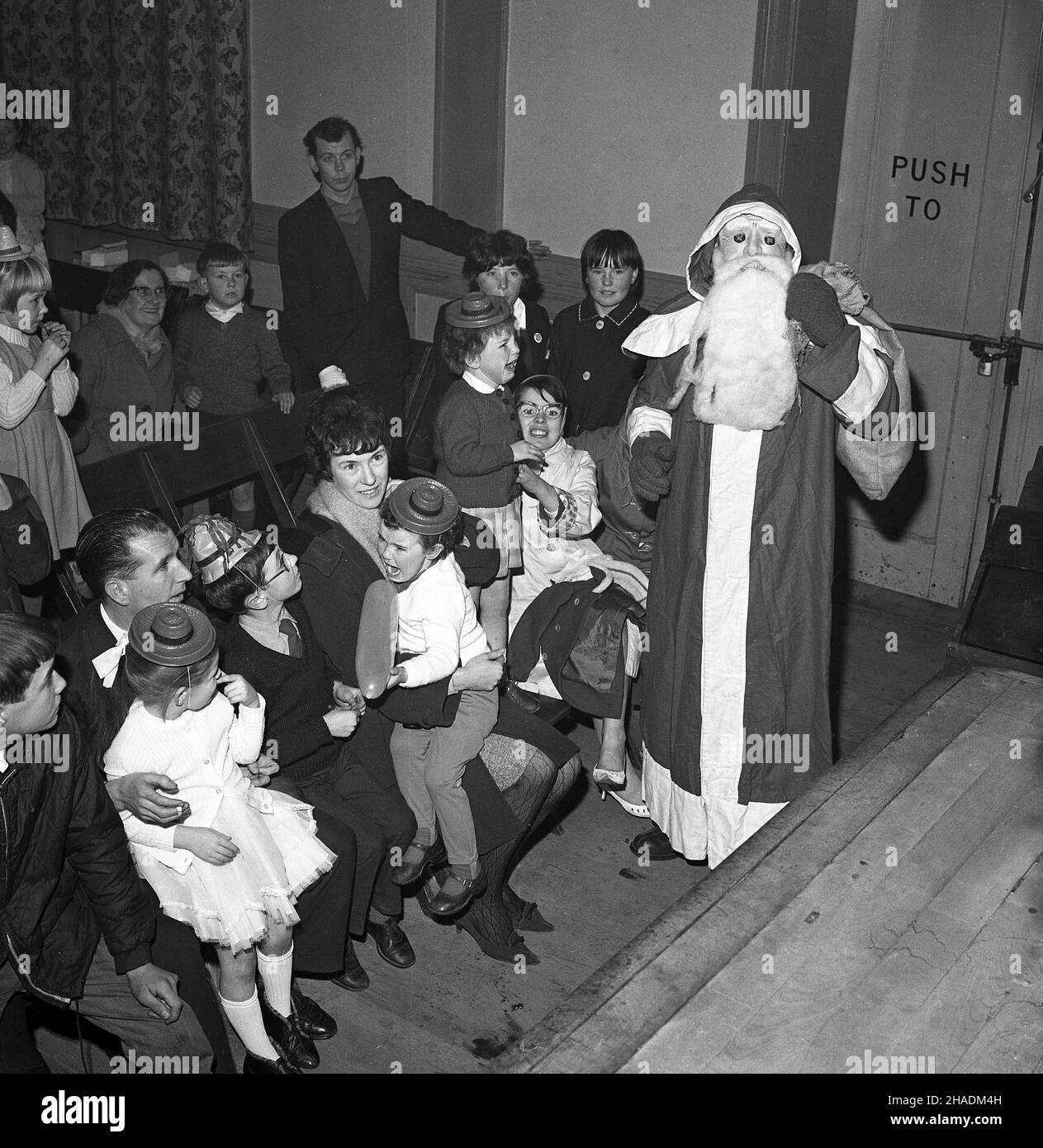 1965, storica, in una sala del villaggio, un babbo natale spaventoso, bambine tenute dai loro genitori spaventato da a babbo natale con una maschera facciale e falsa barba, Fife, Scozia, UK Foto Stock