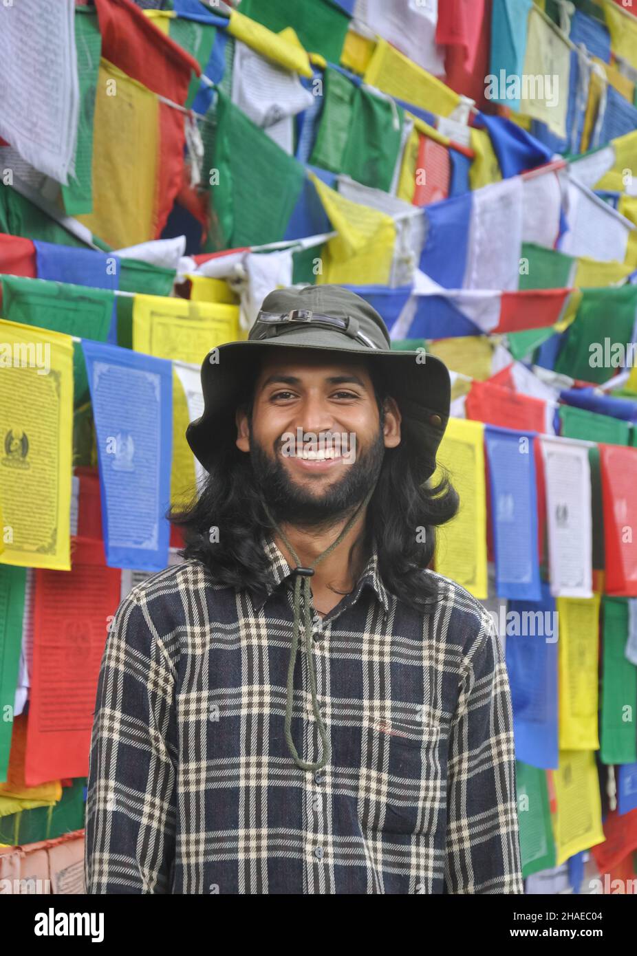 Foto di un turista maschile che guarda la macchina fotografica mentre sorride, in piedi contro le bandiere buddiste di preghiera Foto Stock
