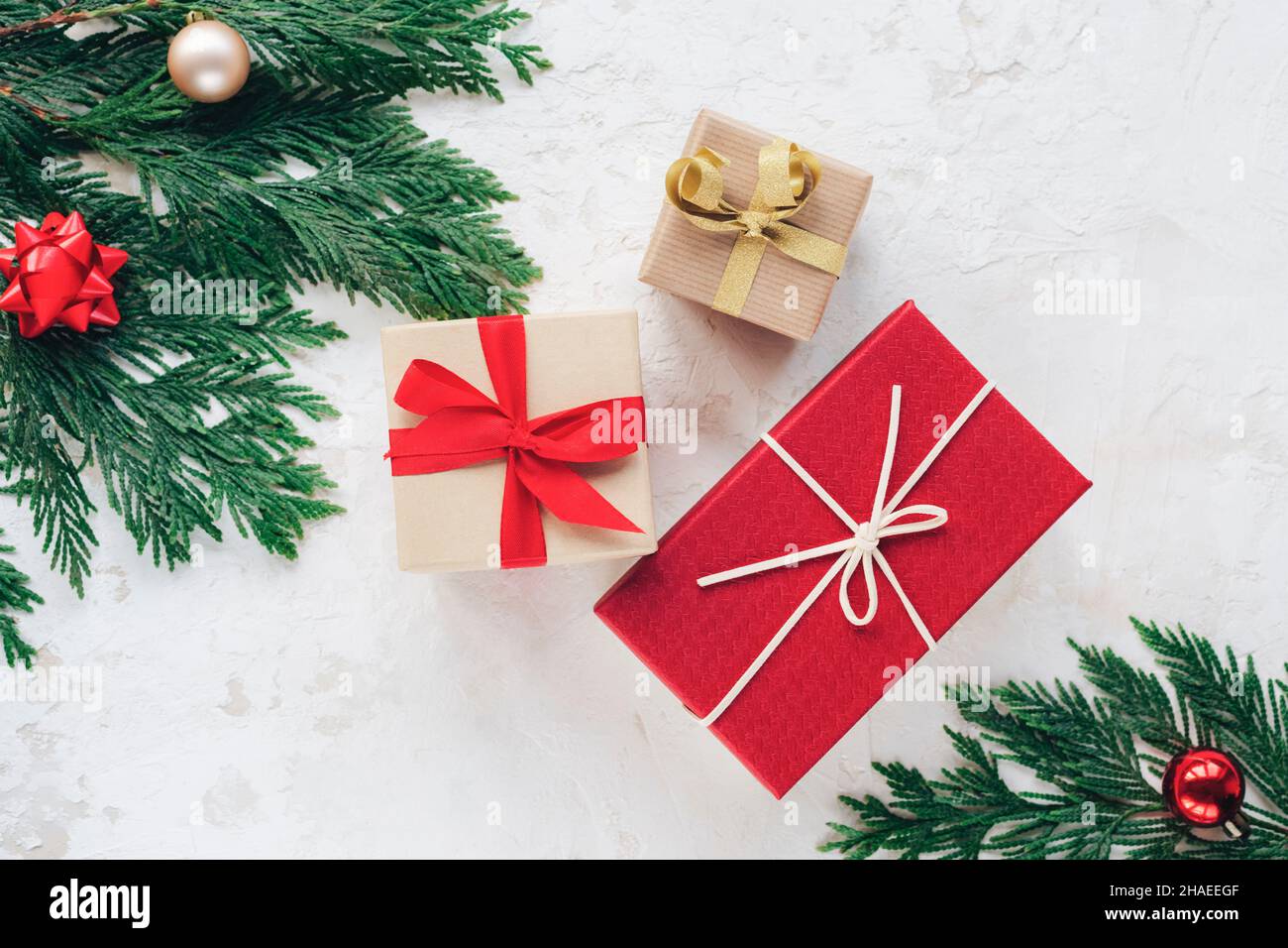 Scatole regalo di Natale, decorate con nastri. Rami di abete con palline rosse e dorate su sfondo bianco testurizzato. Vista dall'alto, piatto. Foto Stock