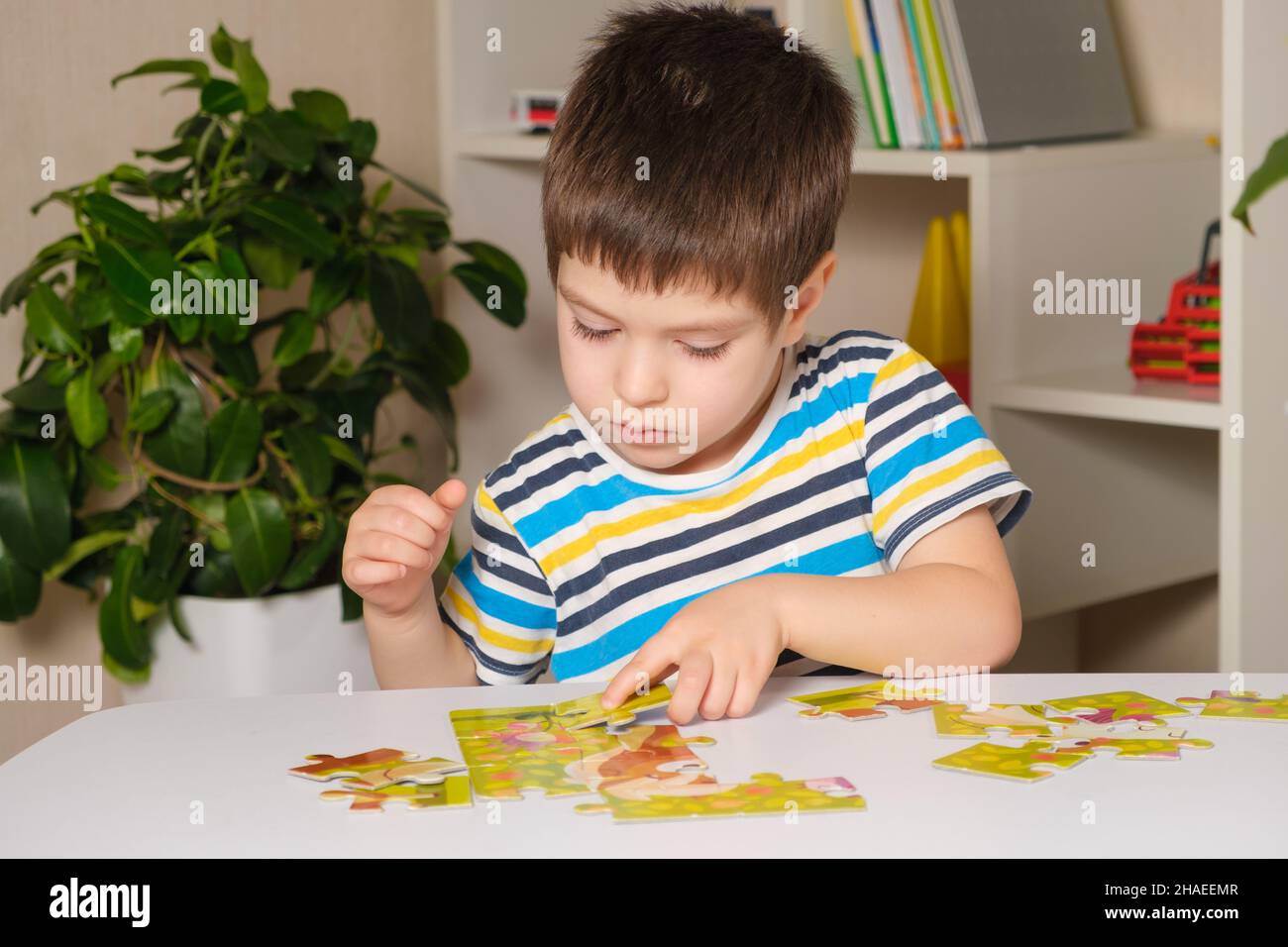 Un ragazzo in una T-shirt a righe gioca puzzle, raccoglie una foto di un cavallo. Foto Stock