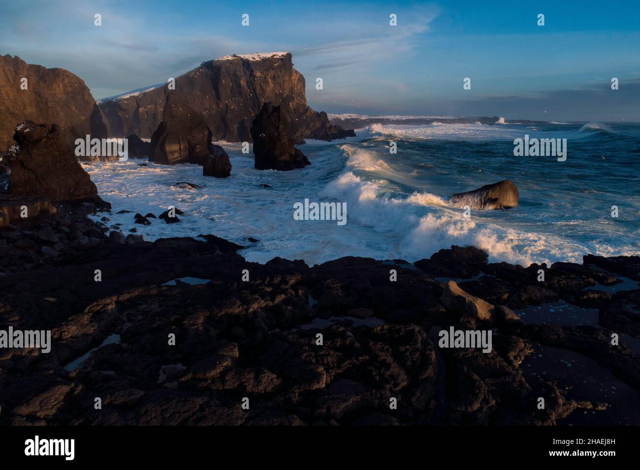 Onde massicce che si infrangono contro grandi formazioni rocciose in Islanda dopo una tempesta invernale nell'oceano Atlantico settentrionale, il tramonto che sbarca dietro la bre Foto Stock