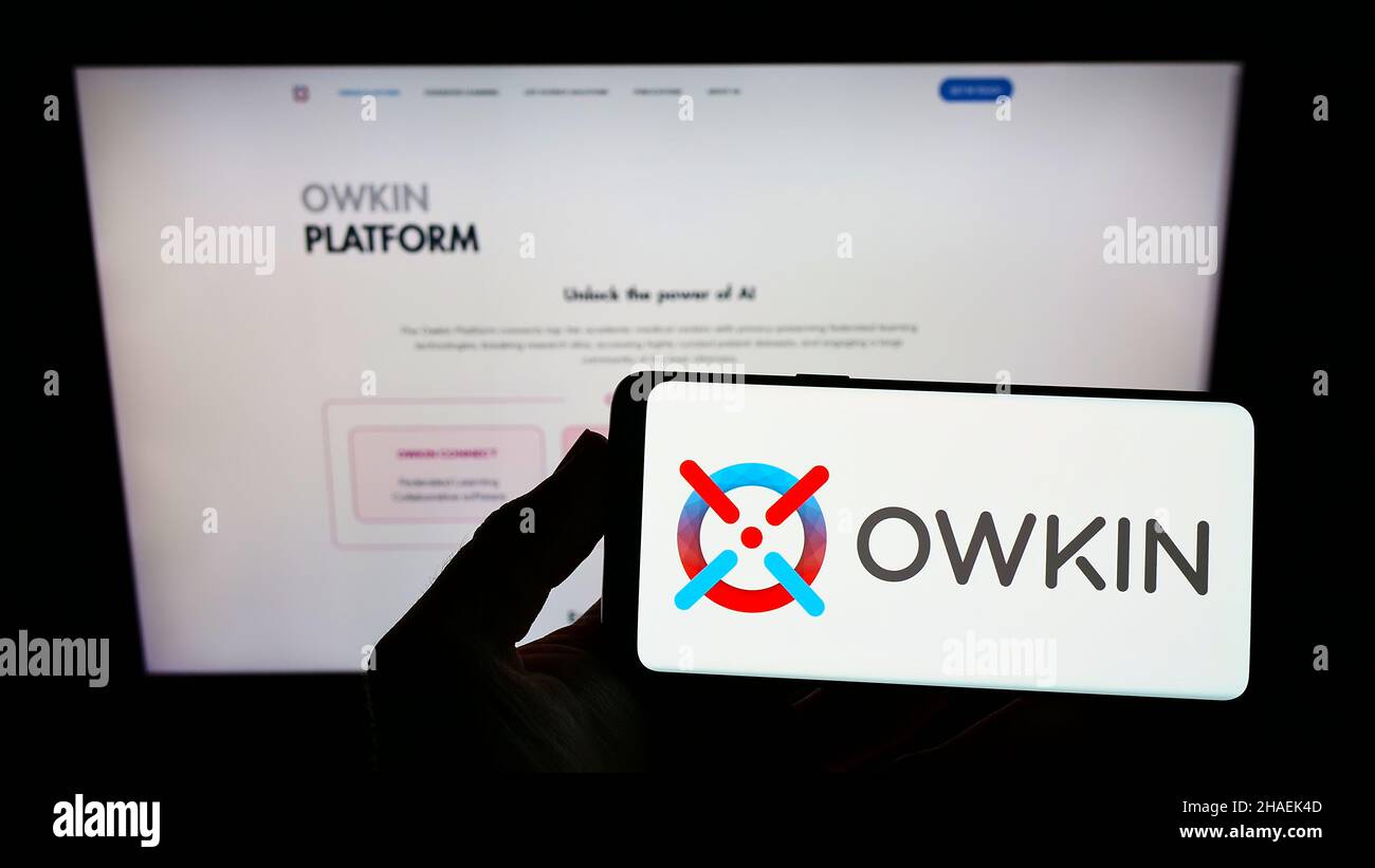 Persona che tiene lo smartphone con il logo della società di ricerca medica statunitense Owkin Inc. Sullo schermo di fronte al sito web. Mettere a fuoco sul display del telefono. Foto Stock